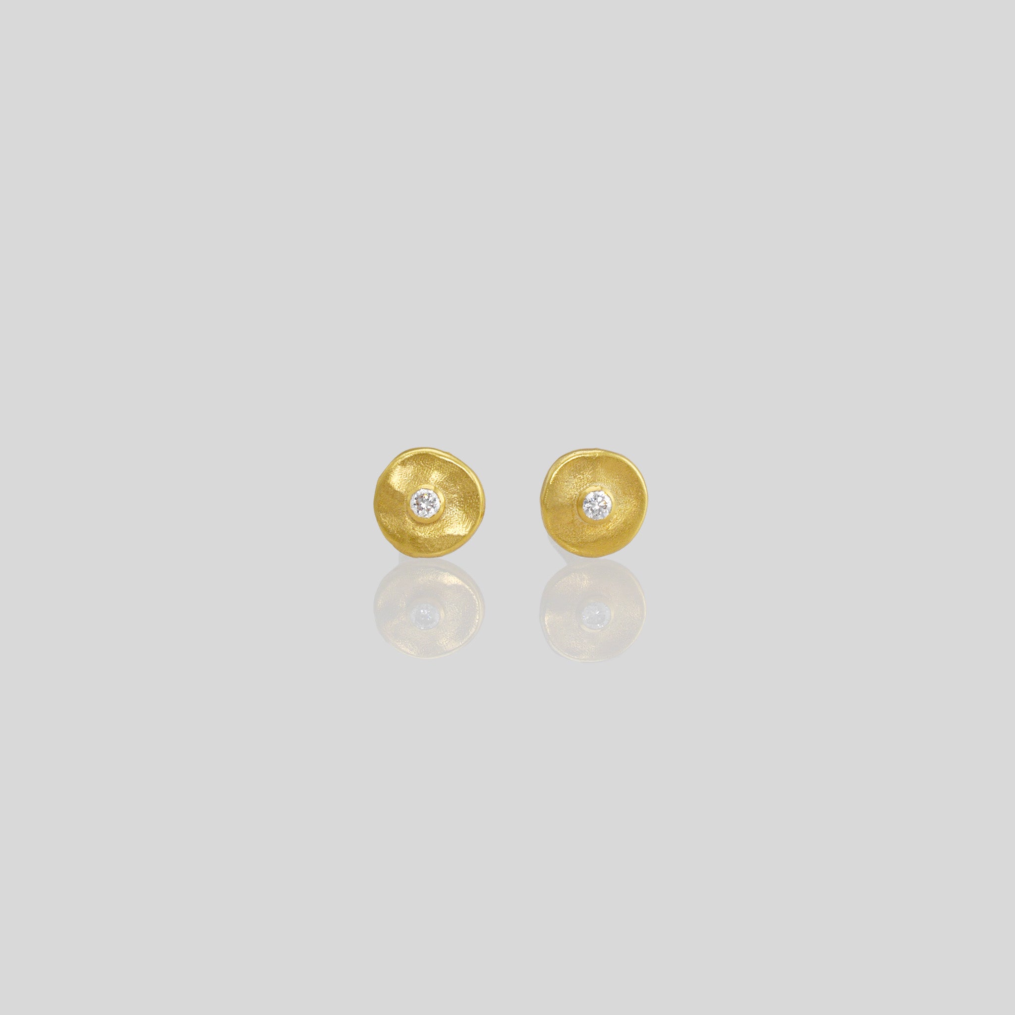Hand-crafted gold stud earrings with a round amorphous shape, featuring a diamond set in the center.