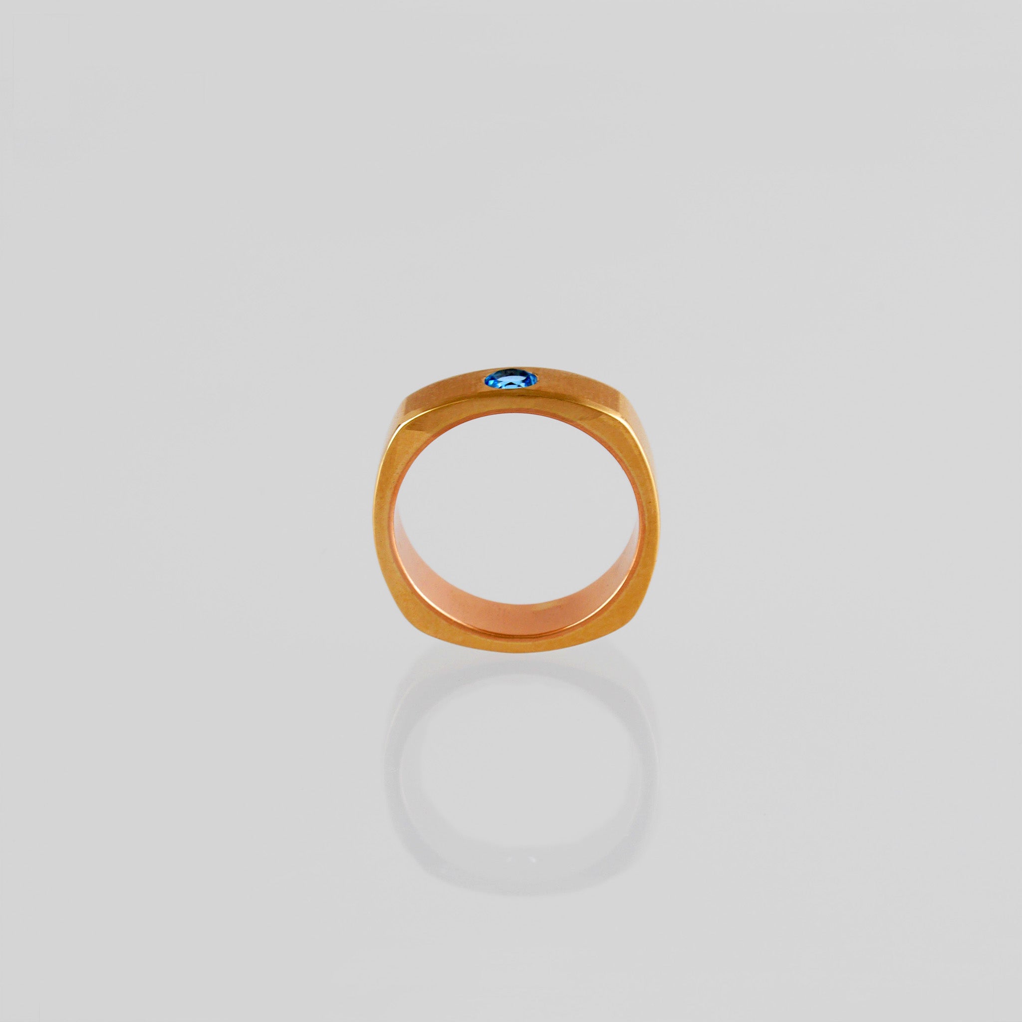 side view of a Square Ring with rounded edges, symbolizing 'rounding the square,' crafted from 18k Rose Gold and adorned with Blue Topaz. A metaphor for overcoming challenges with grace and elegance.
