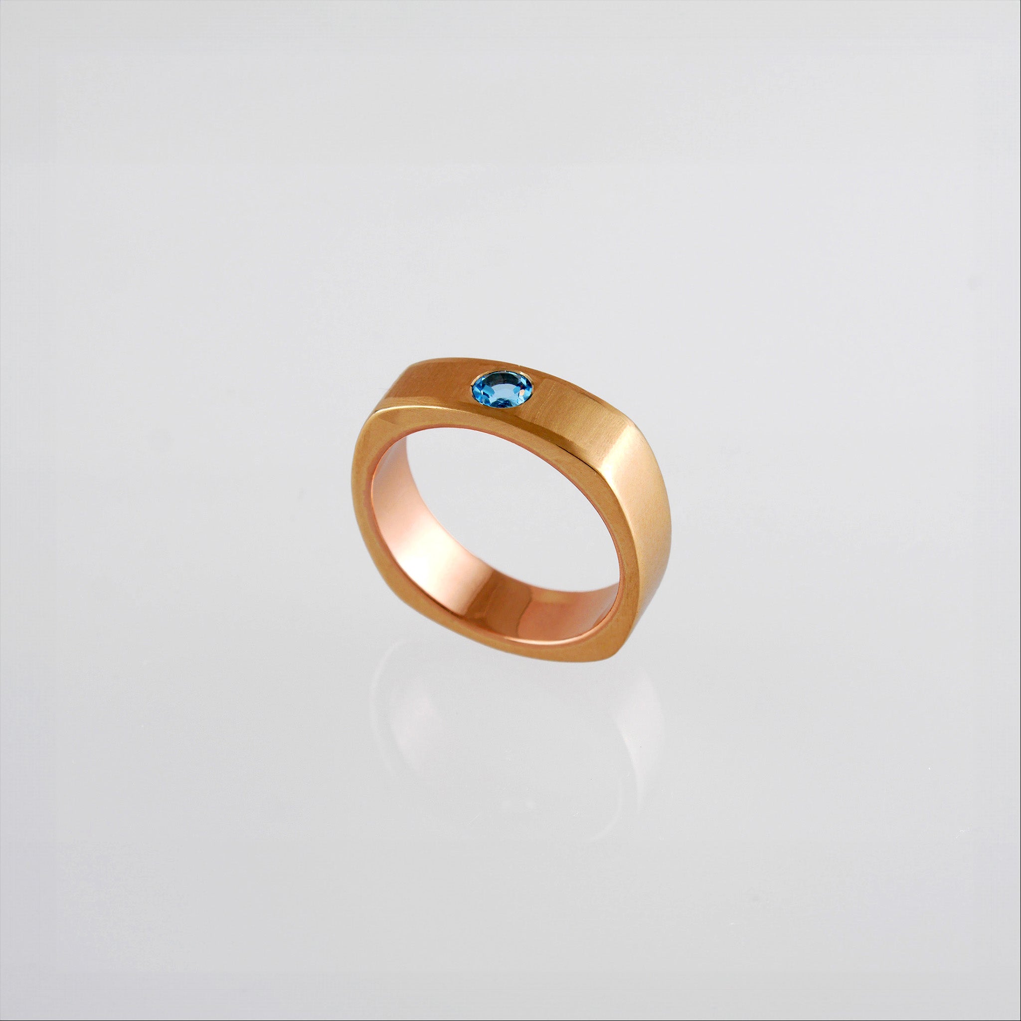 Top view of a Square Ring with rounded edges, symbolizing 'rounding the square,' crafted from 18k Rose Gold and adorned with Blue Topaz. A metaphor for overcoming challenges with grace and elegance.