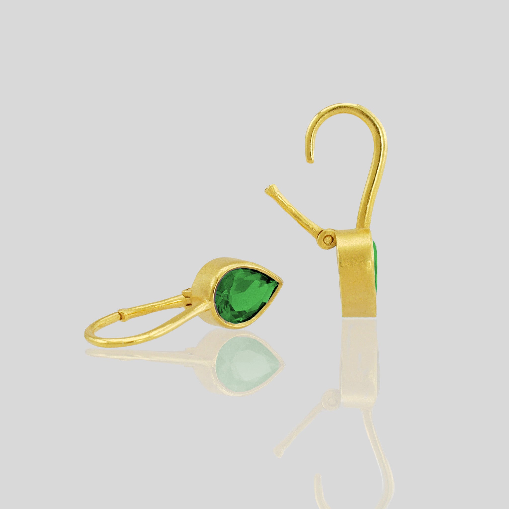 Close up of lightweight 18k gold earrings featuring a drop-shaped Emerald gemstone and promote spiritual harmony