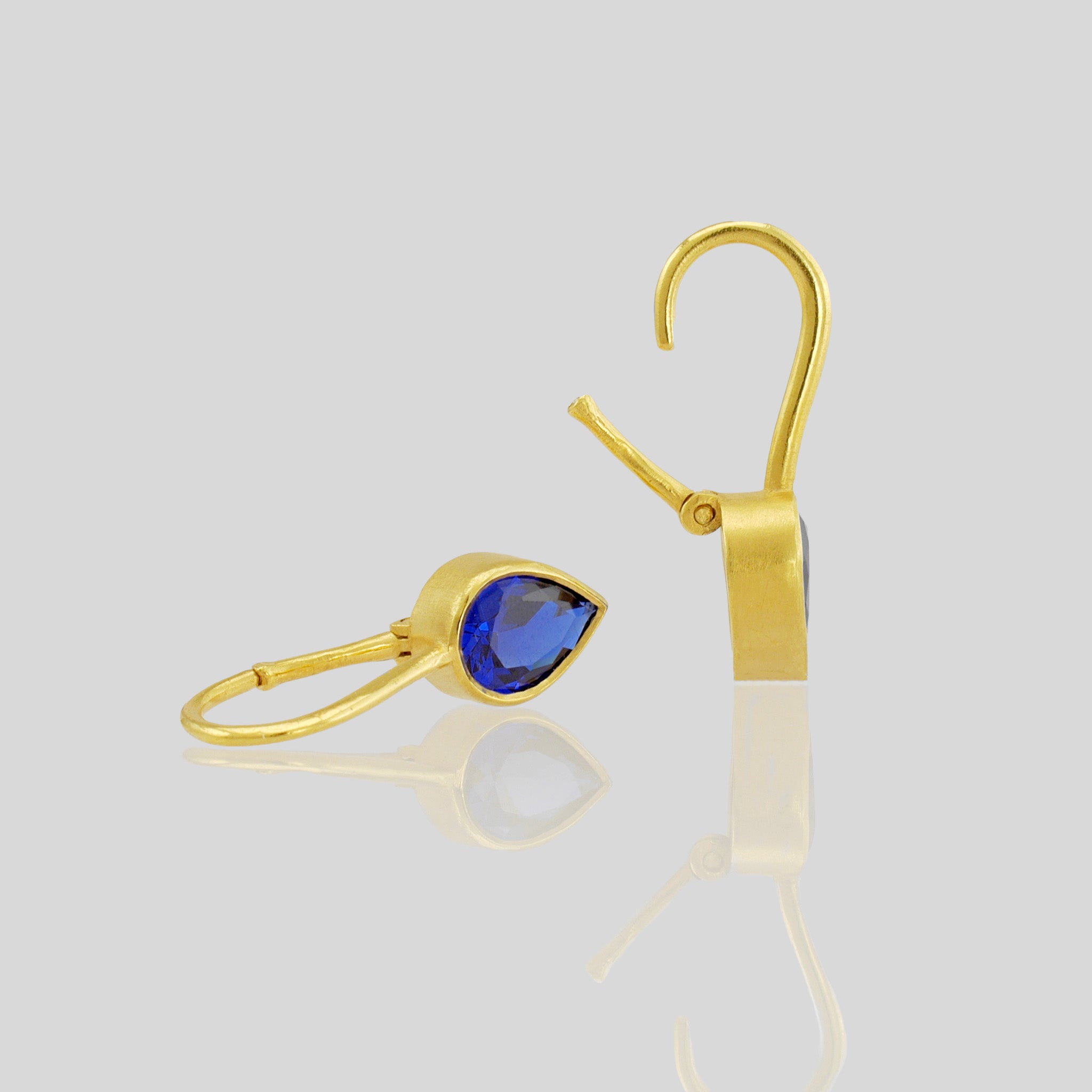 Close up of lightweight gold earrings featuring a drop-shaped Sapphire gemstone and promote spiritual harmony.