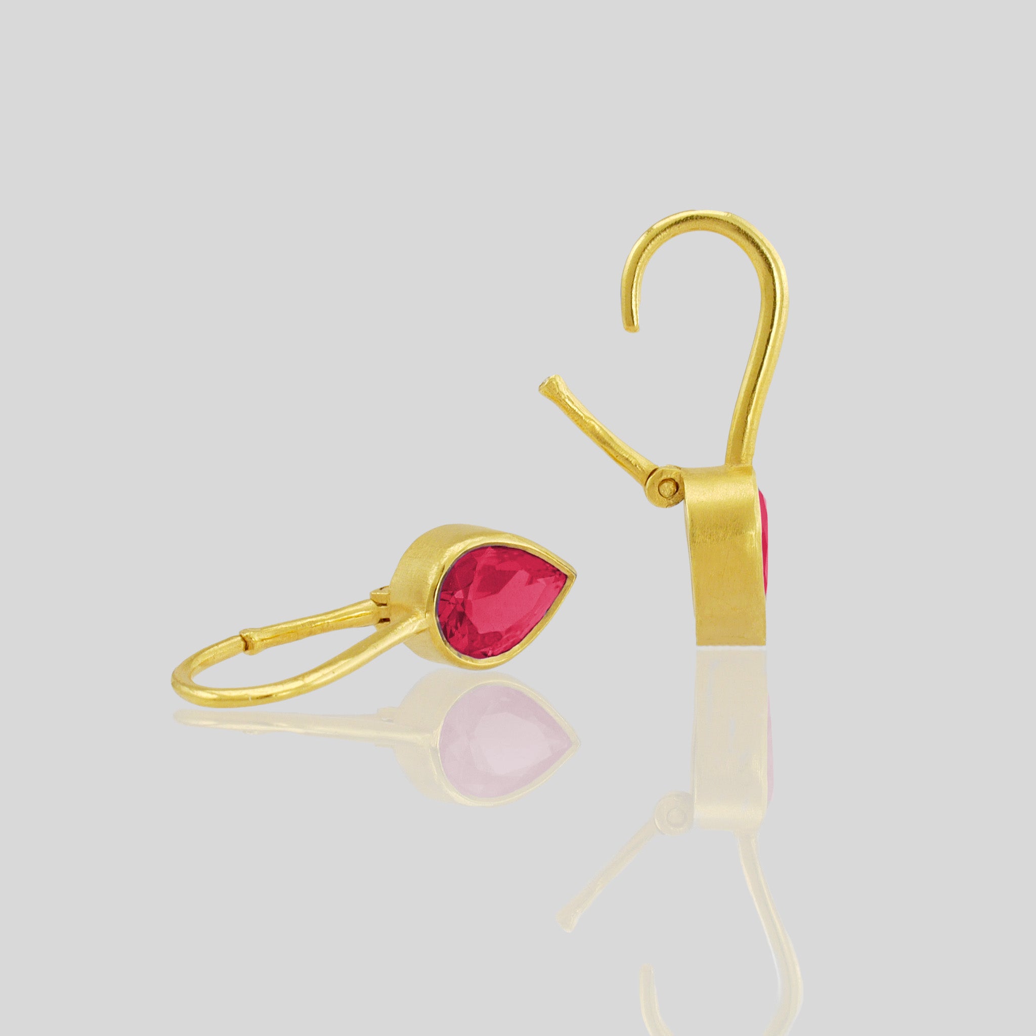 Closeup of lightweight gold earrings featuring a drop-shaped Ruby gemstone and promote spiritual harmony