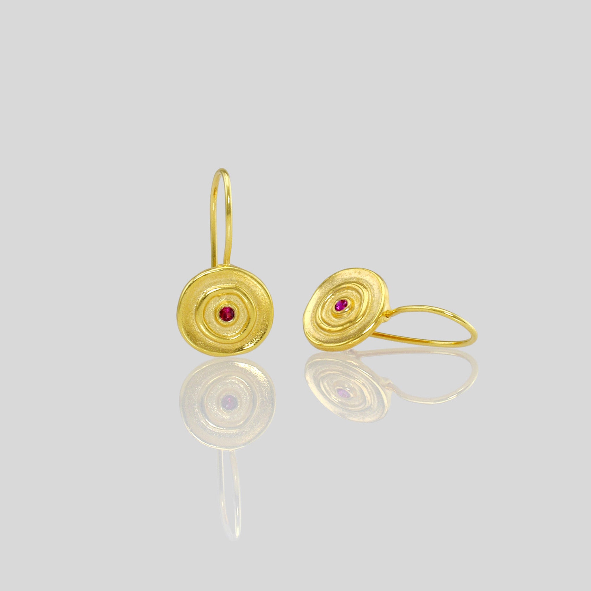 Close up of Hand-made round drop earrings with yellow gold and a central Ruby gemstone, inspired by ancient Egyptian Pharaohs' gold jewelry.