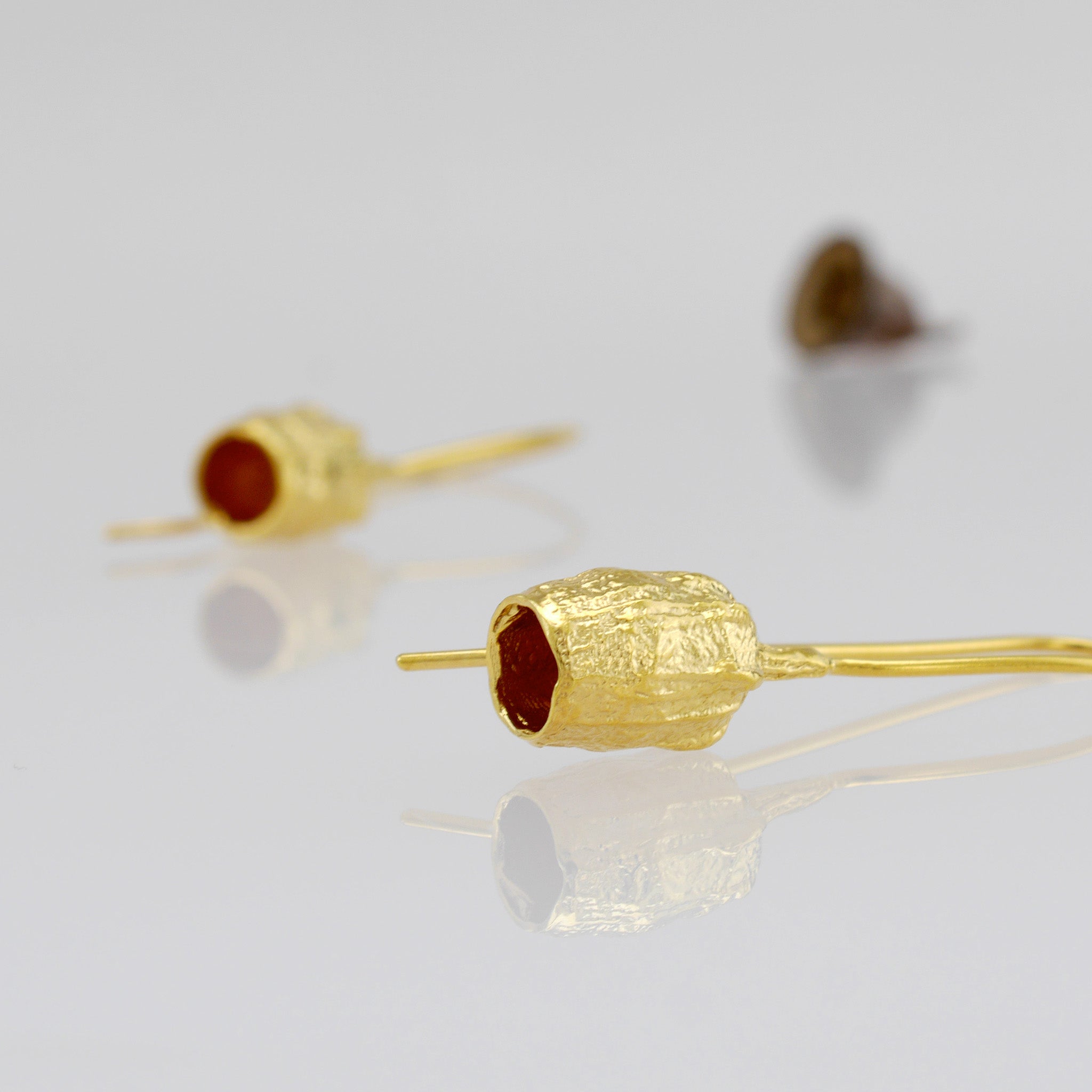 Gold drop earrings featuring a bell-shaped seed, which is a replica of a dried seed collected from nature.
