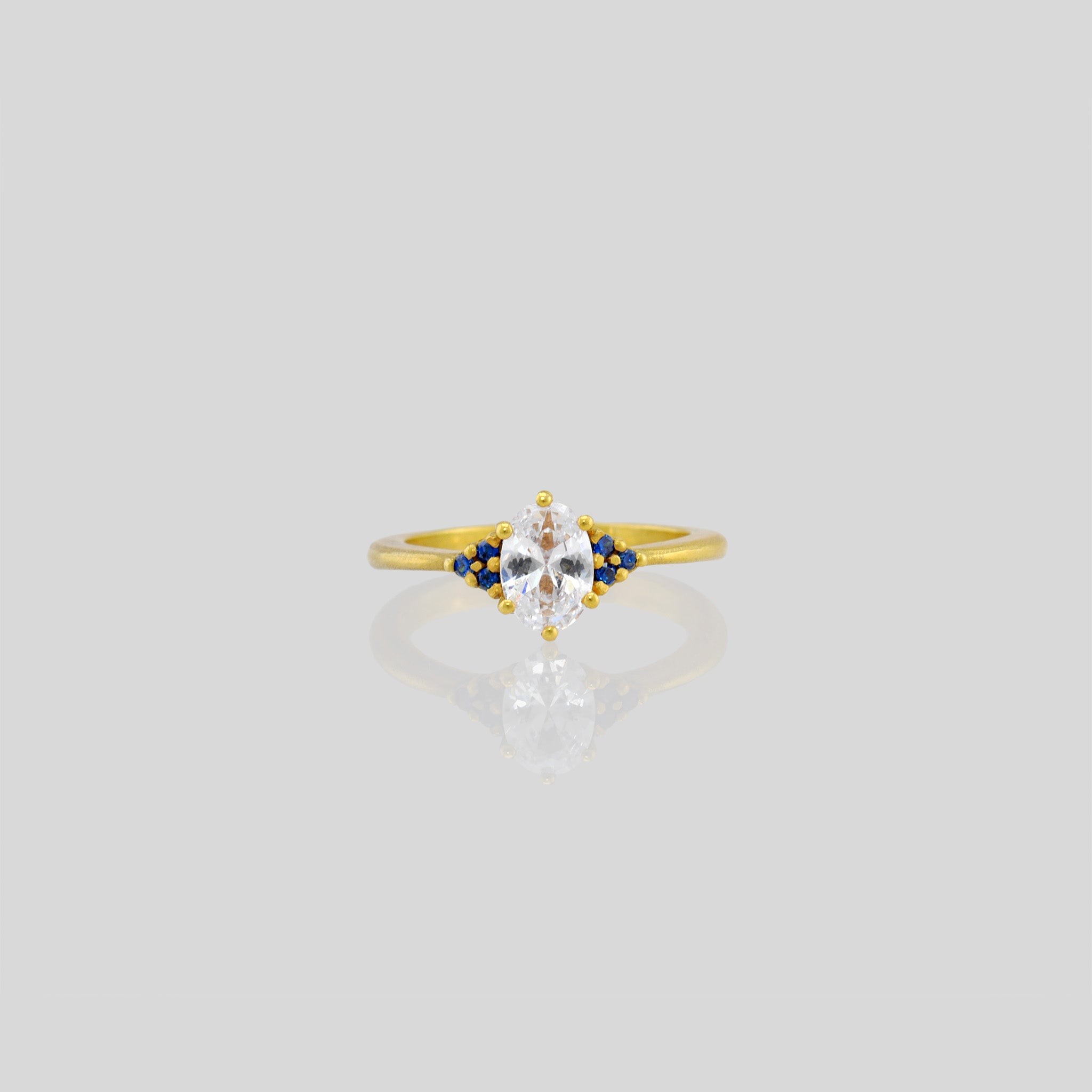 Front angle of our Gold engagement ring with oval central diamond and three tiny Sapphires on each side. Timeless elegance with a touch of color, perfect for an elegant proposal.