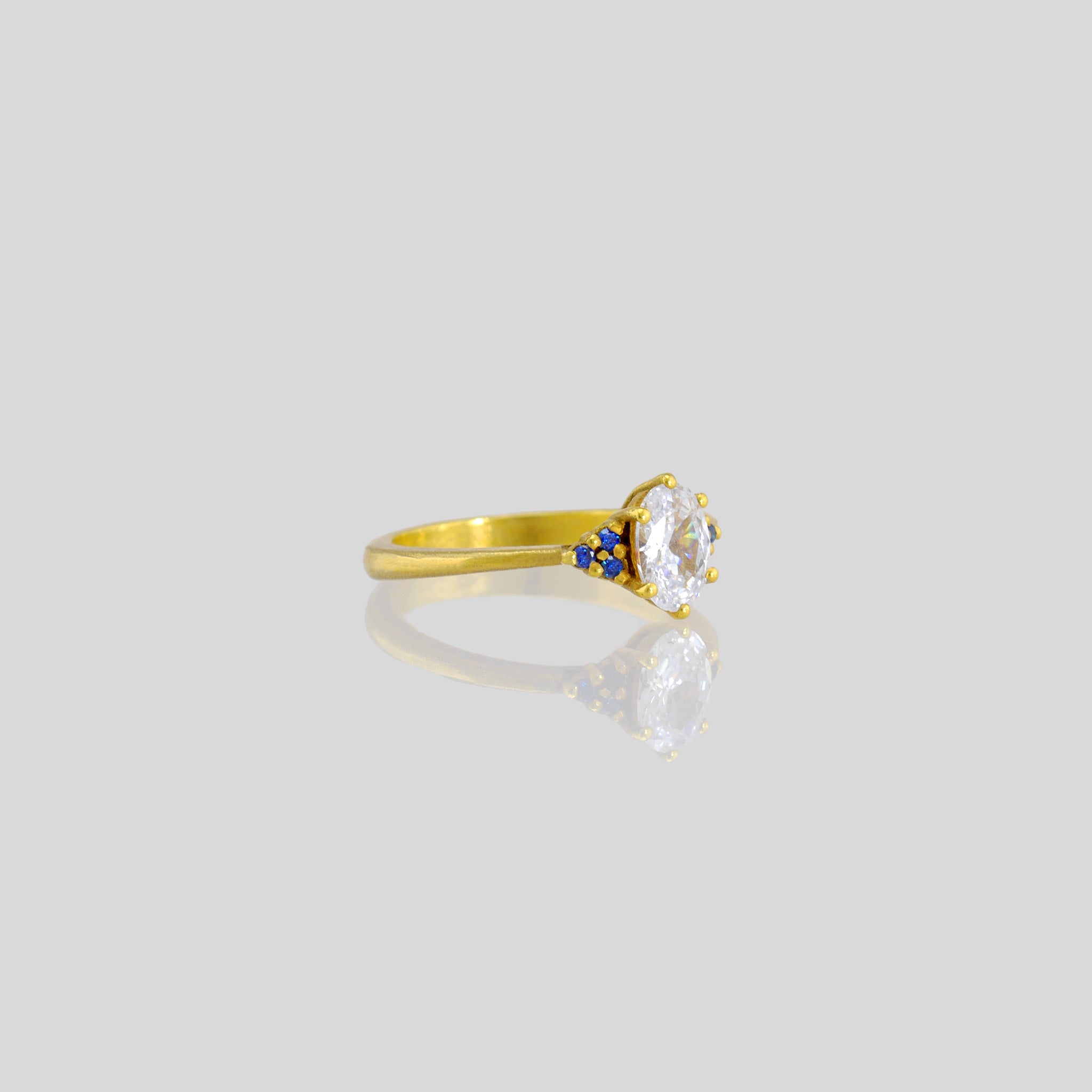 Gold engagement ring with oval central diamond and three tiny Sapphires on each side. Timeless elegance with a touch of color, perfect for an elegant proposal.