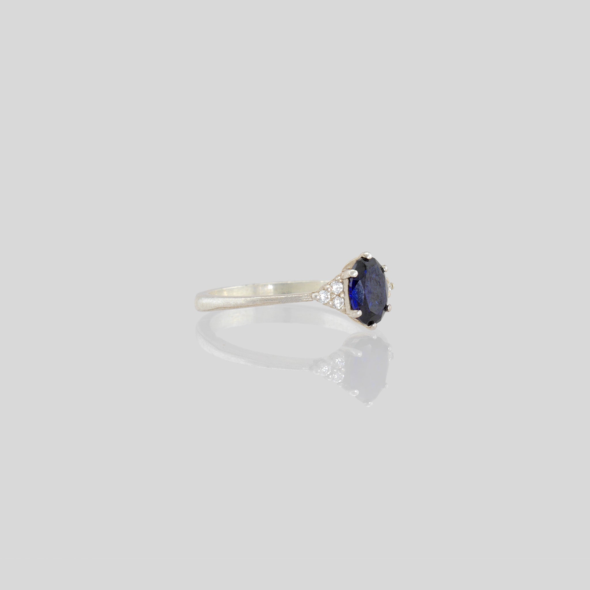 White Gold engagement ring featuring an oval central Sapphire and three dainty Diamonds on each side, offering timeless elegance with added sparkle.