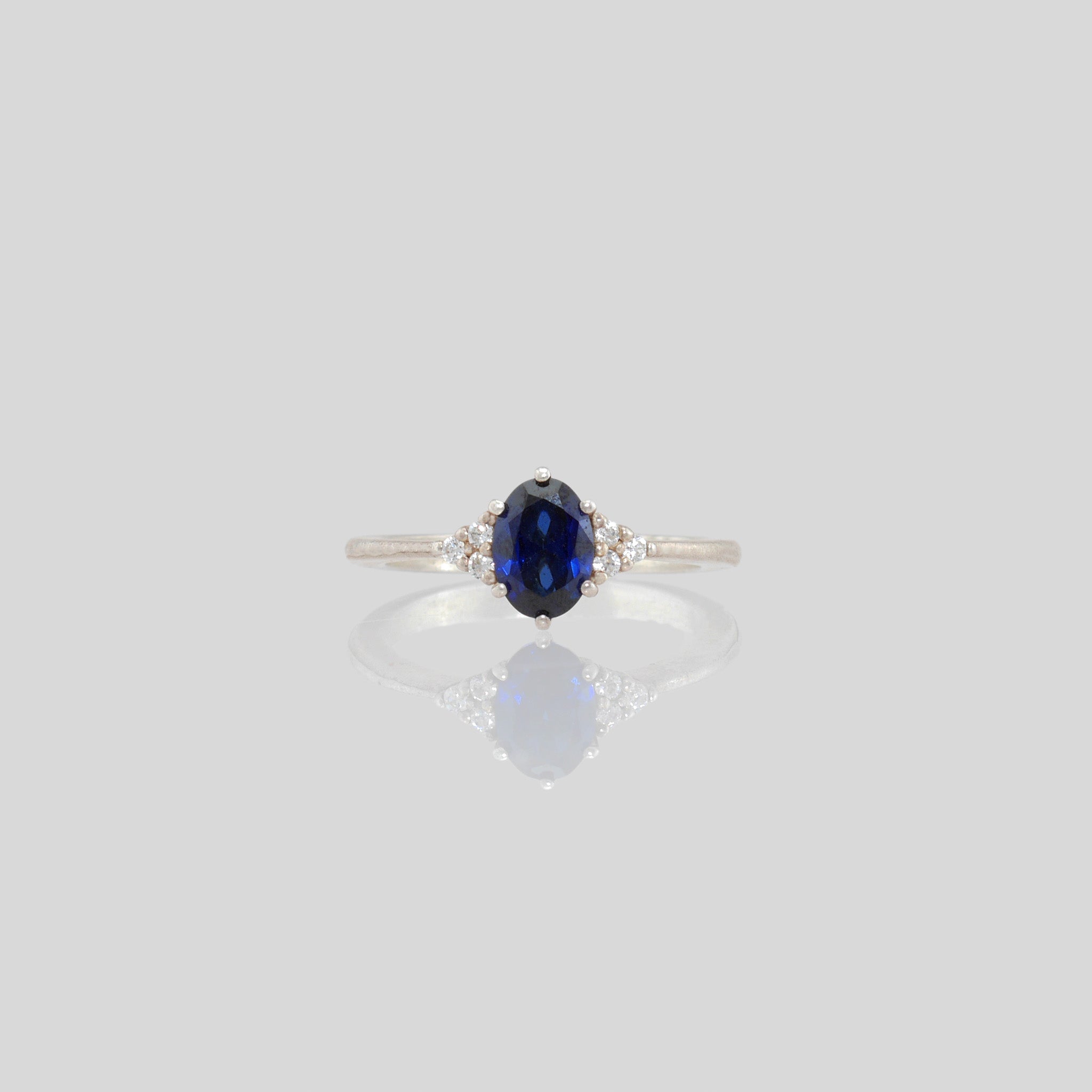 Front view of our White Gold engagement ring featuring an oval central Sapphire and three dainty Diamonds on each side, offering timeless elegance with added sparkle.