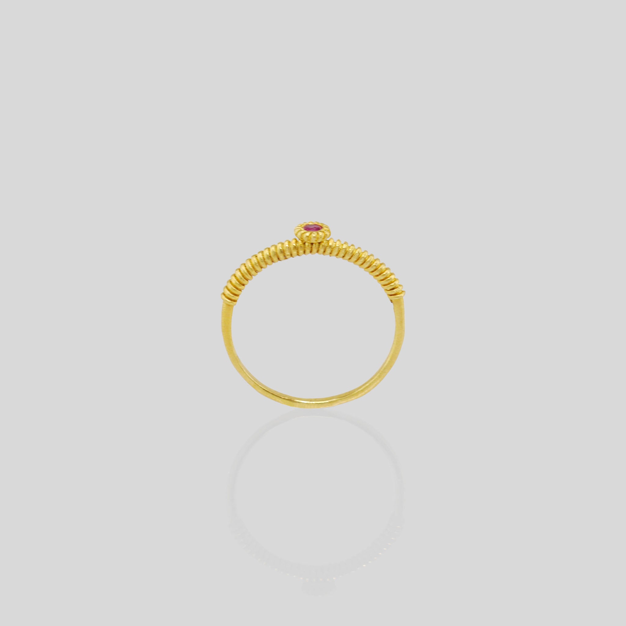 Side view of a thin gold ring with a coiled gold string, showcasing a vivid Ruby at its center. Elegant and charming, it radiates subtle allure.