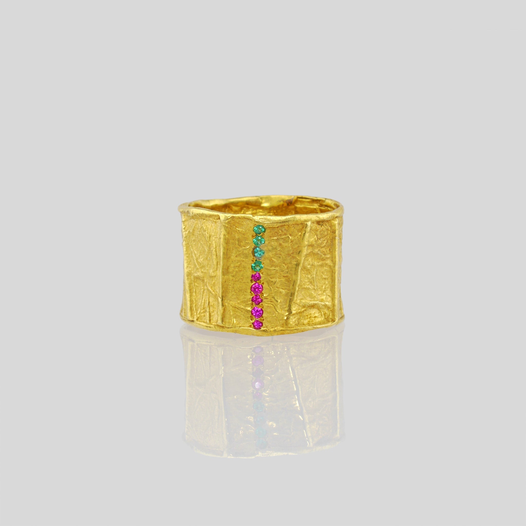 Handcrafted gold ring featuring a wide band with a distinct textured surface achieved through Kami's paper modeling technique. Embellished with miniature rubies and emeralds, this ring exudes a one-of-a-kind, magnificent charm.