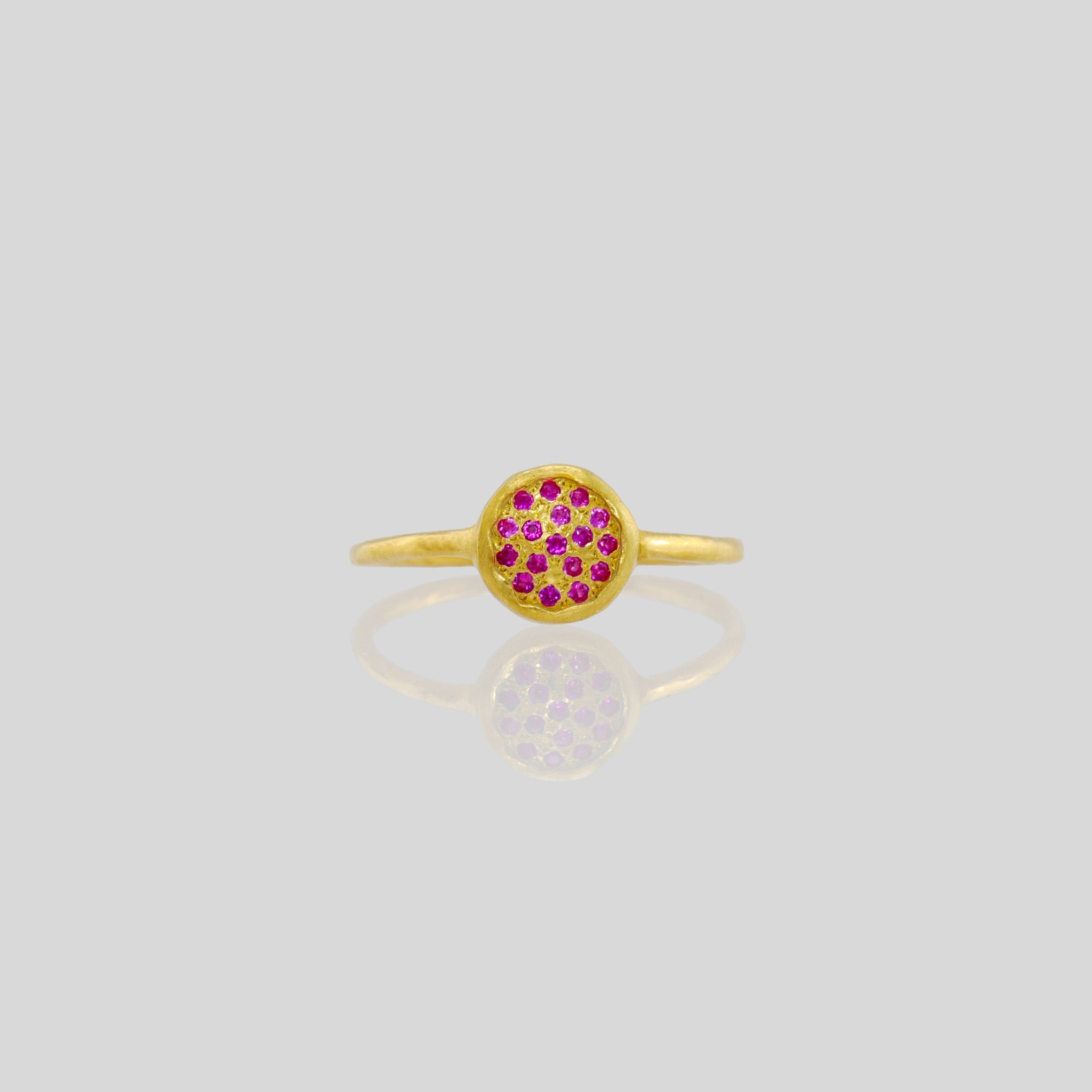 Front view of a Delicate hand-made gold ring with a circular plate set with tiny Ruby gemstones. The sparkle from the stones resembles a starry night.