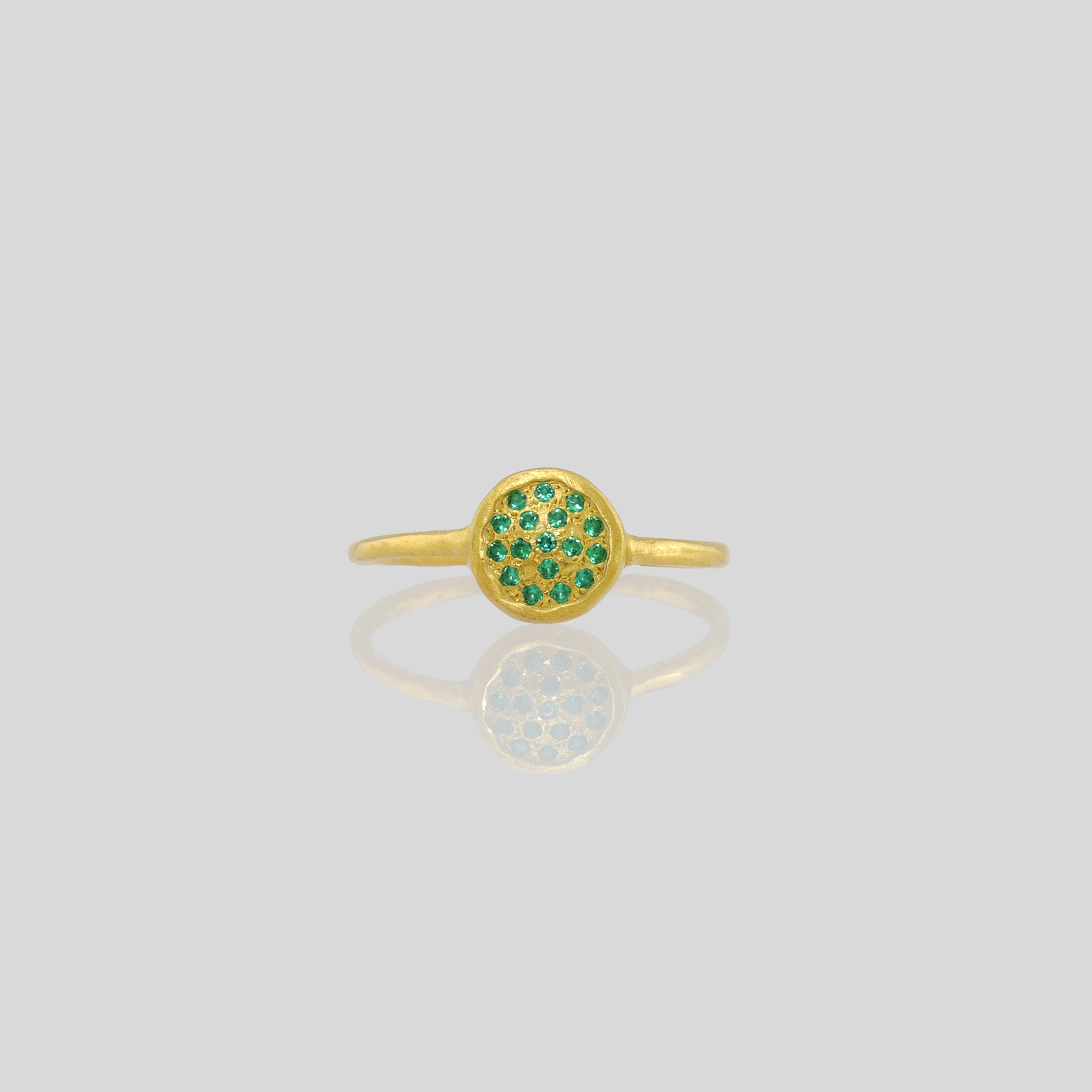 Front view of a Delicate hand-made gold ring with a circular plate set with tiny Emerald gemstones. The sparkle from the stones resembles a starry night. 