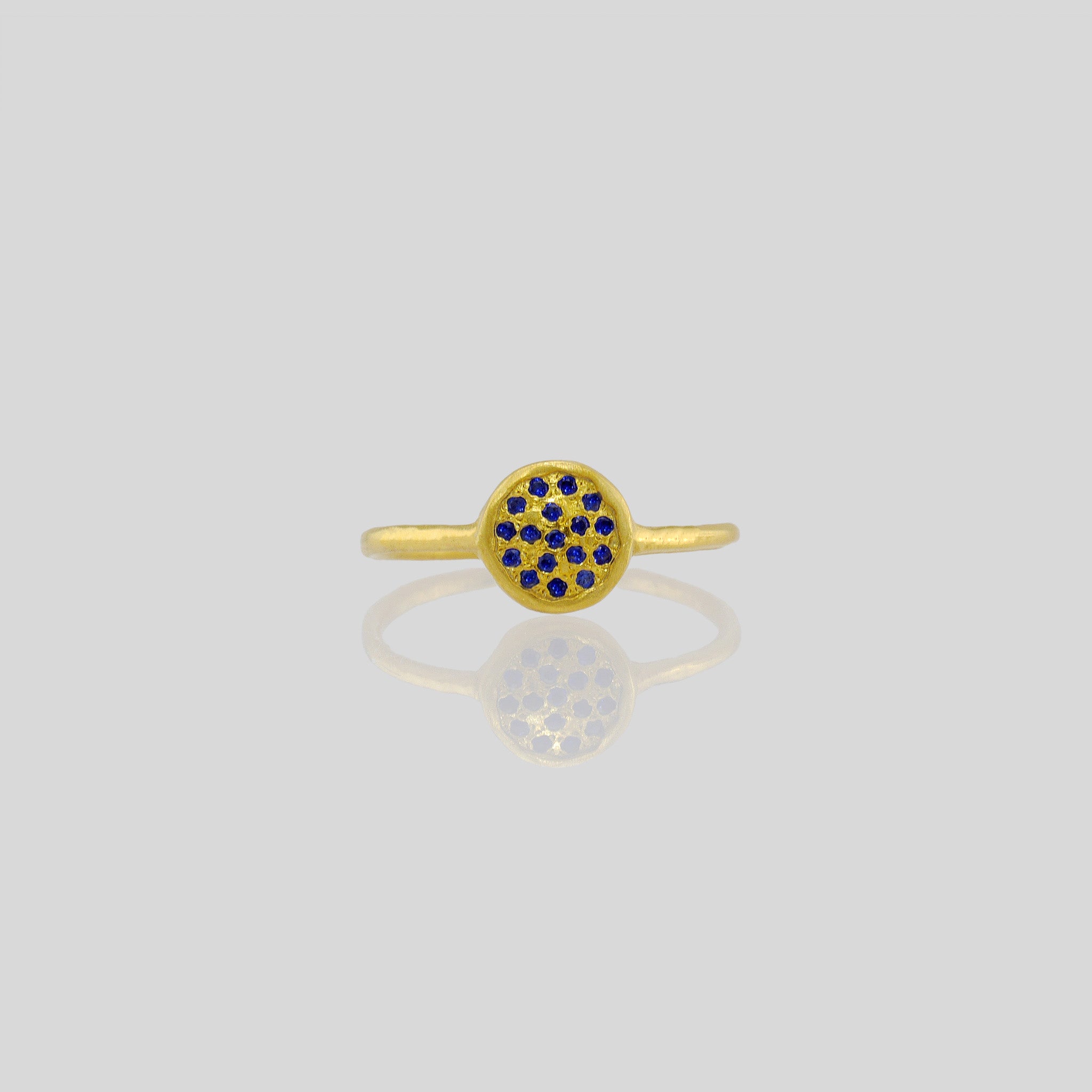 Front view of a Delicate hand-made gold ring with a circular plate set with tiny Sapphires. The sparkle from the stones resembles a starry night. 