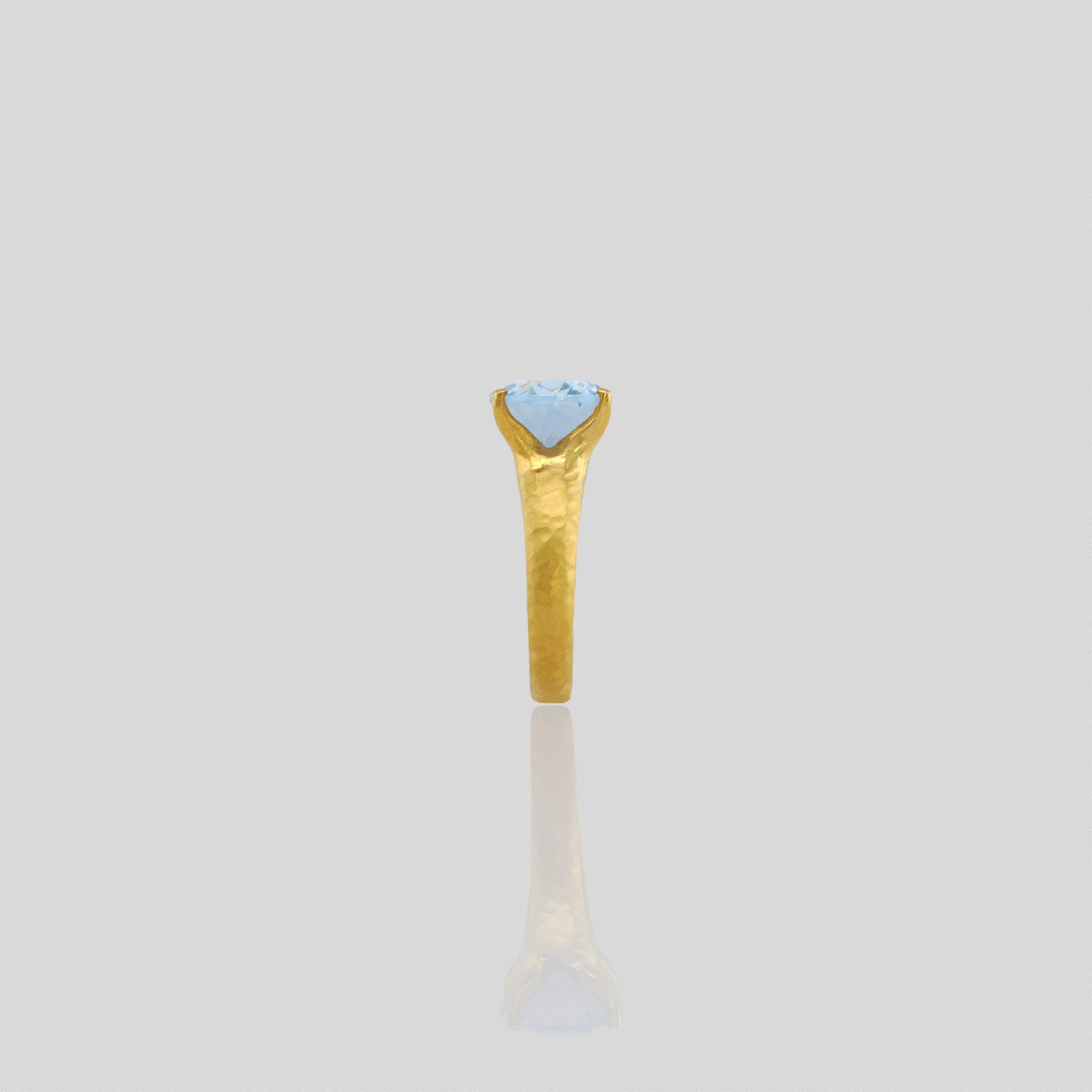 Side view of 18k Gold ring featuring four stems holding an elliptic Blue Topaz, combining rich color depth with a dignified presence.