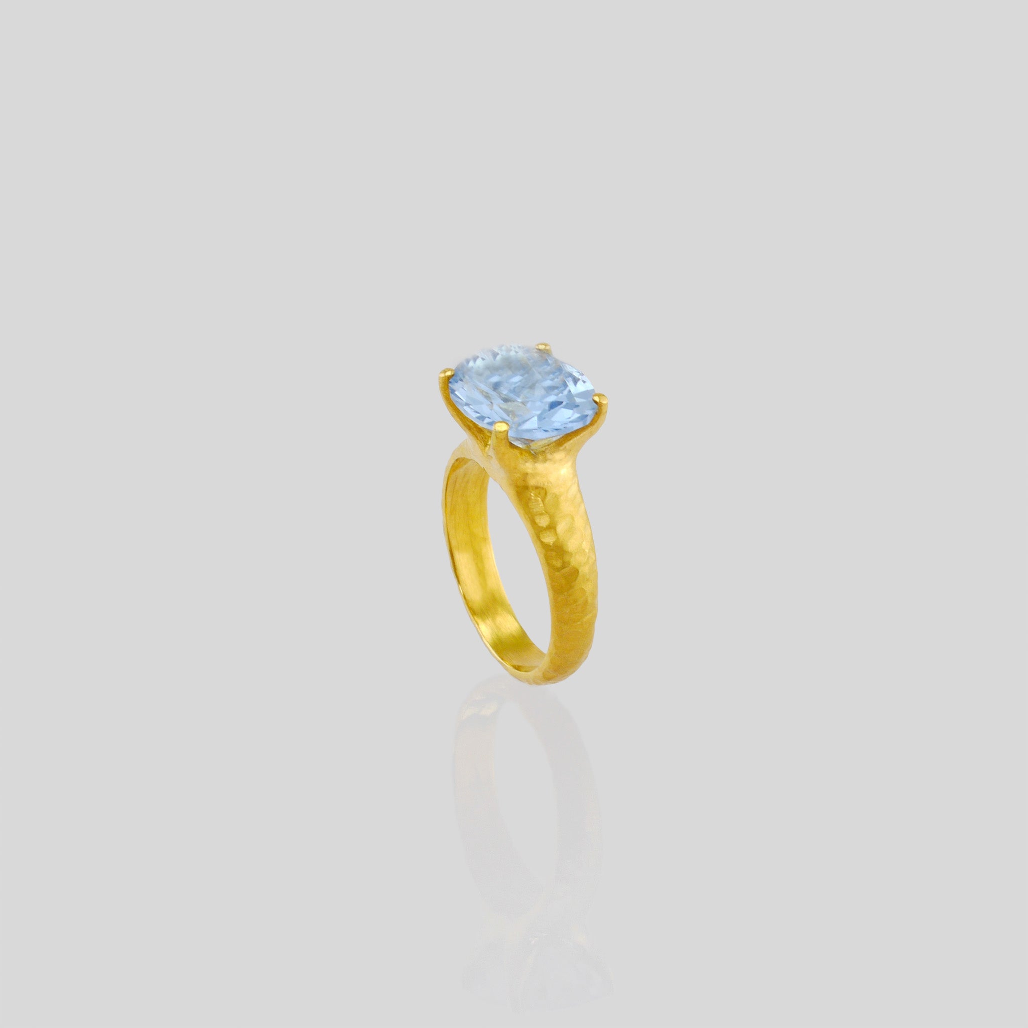 top view of 18k Gold ring featuring four stems holding an elliptic Blue Topaz, combining rich color depth with a dignified presence.