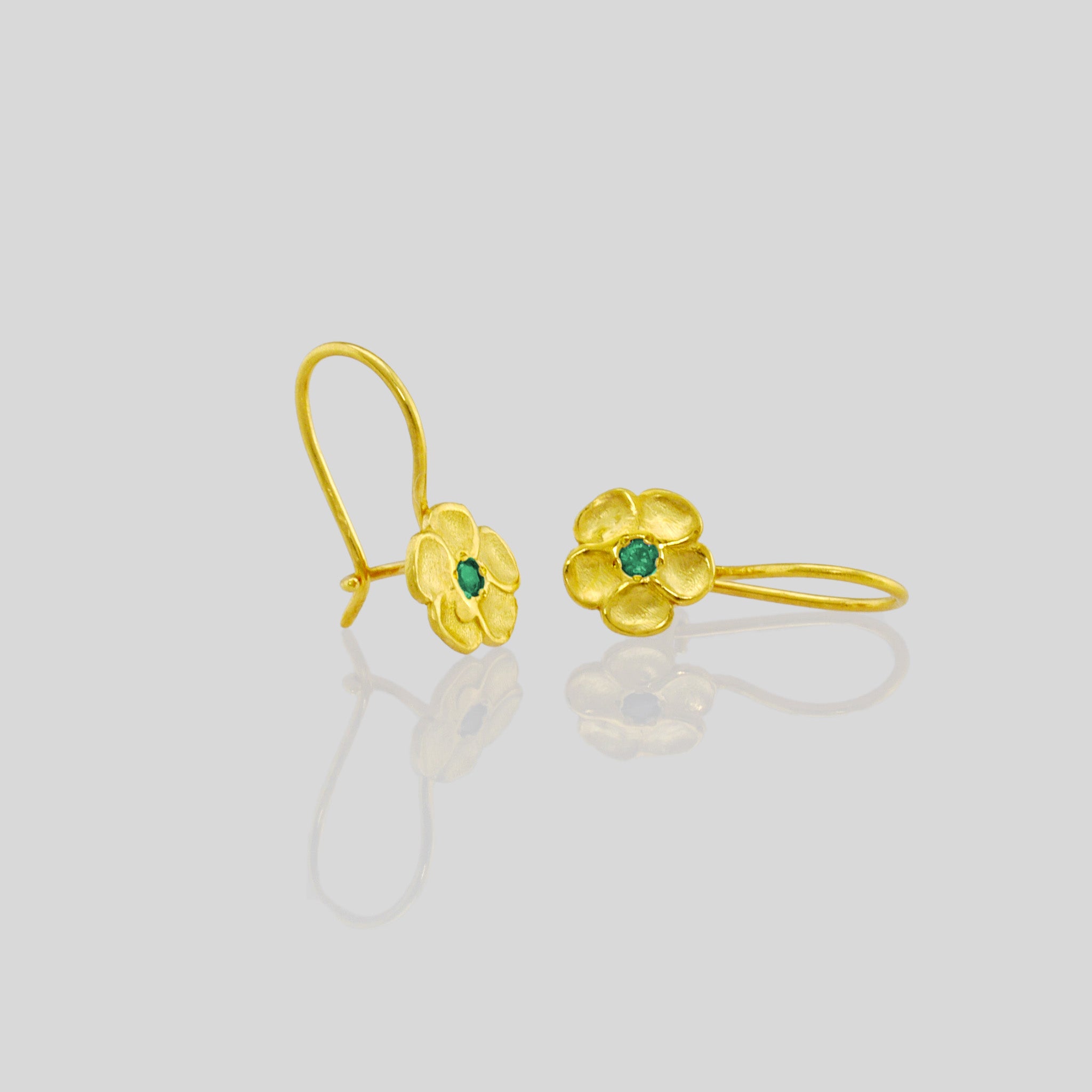 close up of delicate yellow gold flower drop earrings with a sparkling Emerald center. Perfect for any occasion!