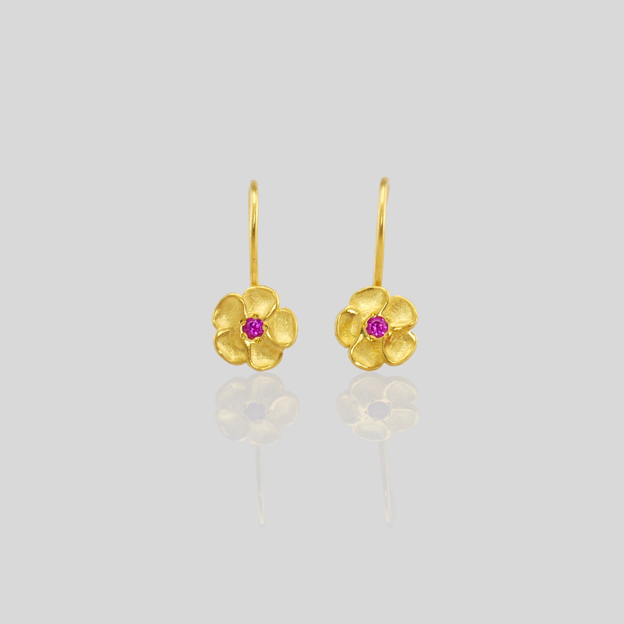 Close up of delicate yellow gold flower drop earrings with a sparkling ruby center. Perfect for any occasion!