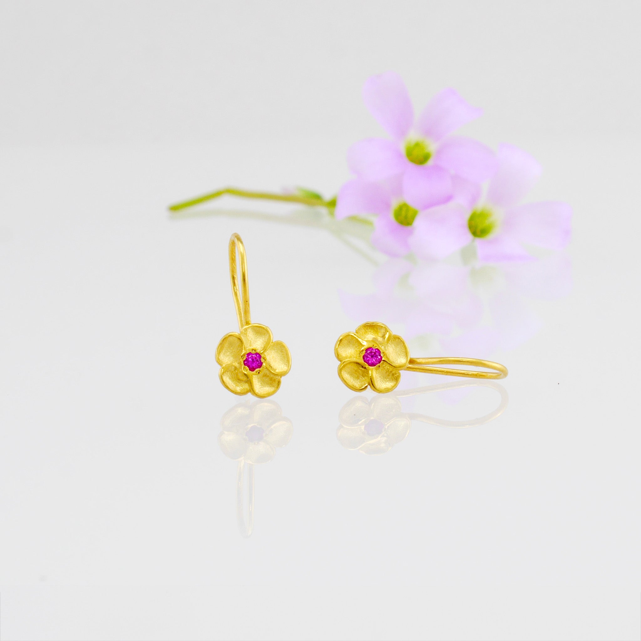 Delicate yellow gold flower drop earrings with a sparkling ruby center. Perfect for any occasion!