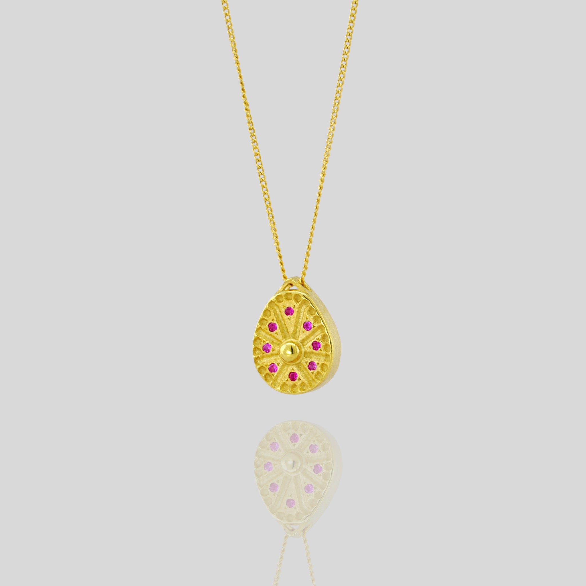 Close up of 18k Gold pendant resembling a Sundial clock, accented with small Rubies between the edges of each clock hand. A luxurious and timeless addition to any collection.