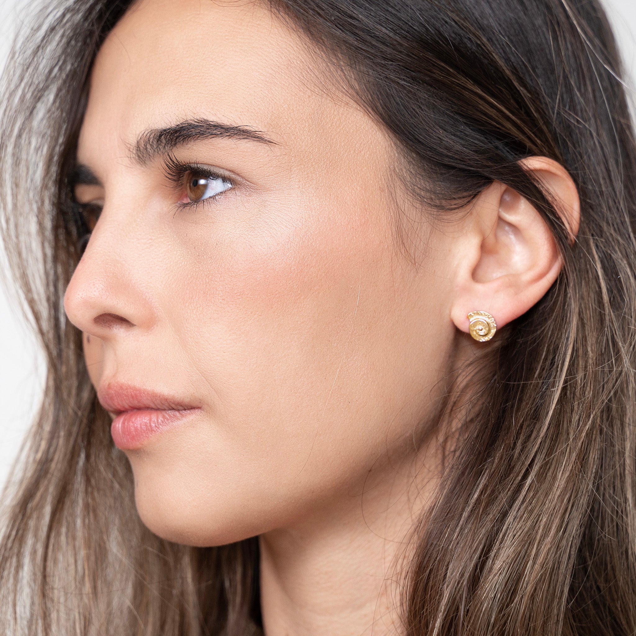Classic and elegant yellow gold stud earrings with a textured arched spiral on a model. 
