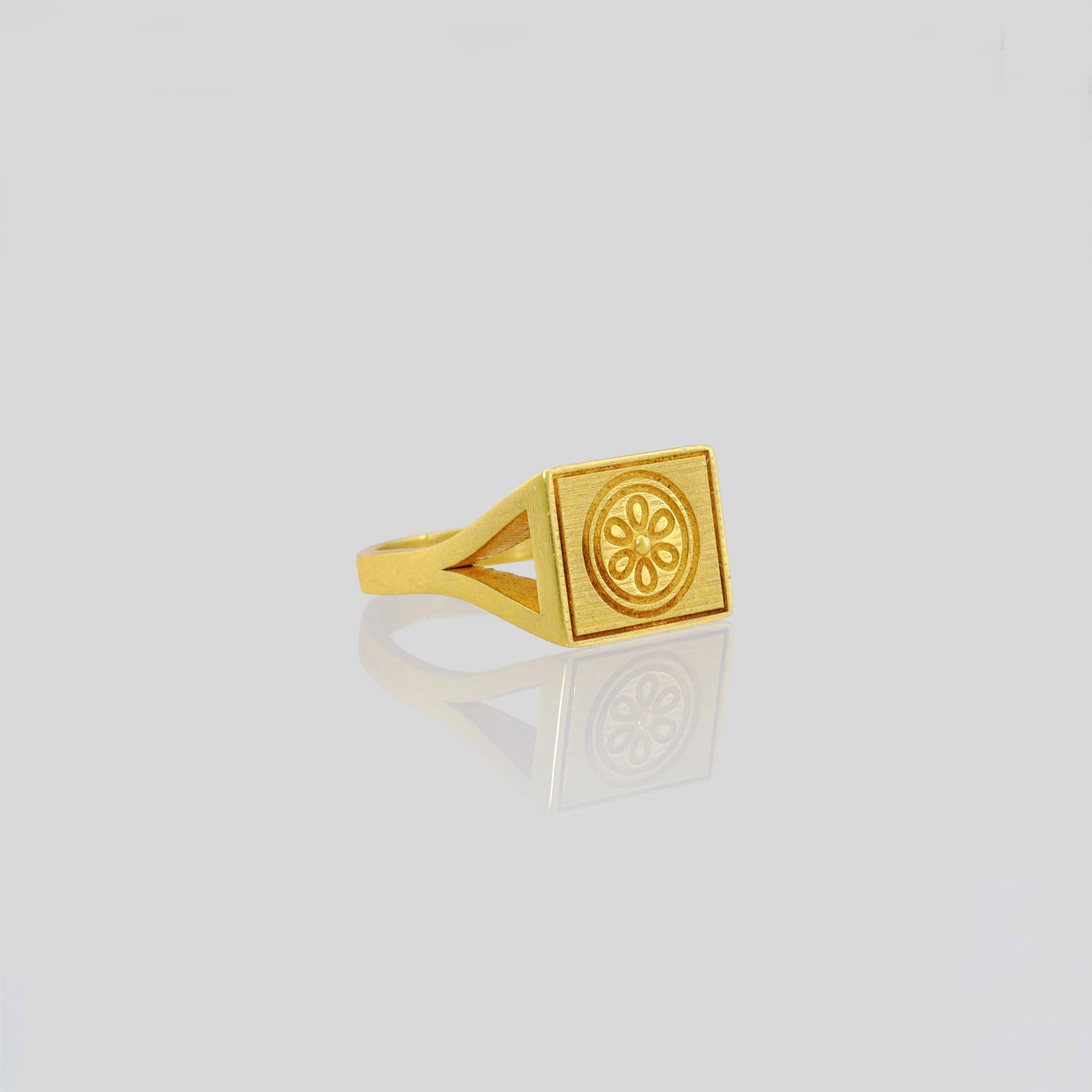 Elegant 18k gold signet ring with a square top featuring an embossed flower design, showcased against a reflective white background.