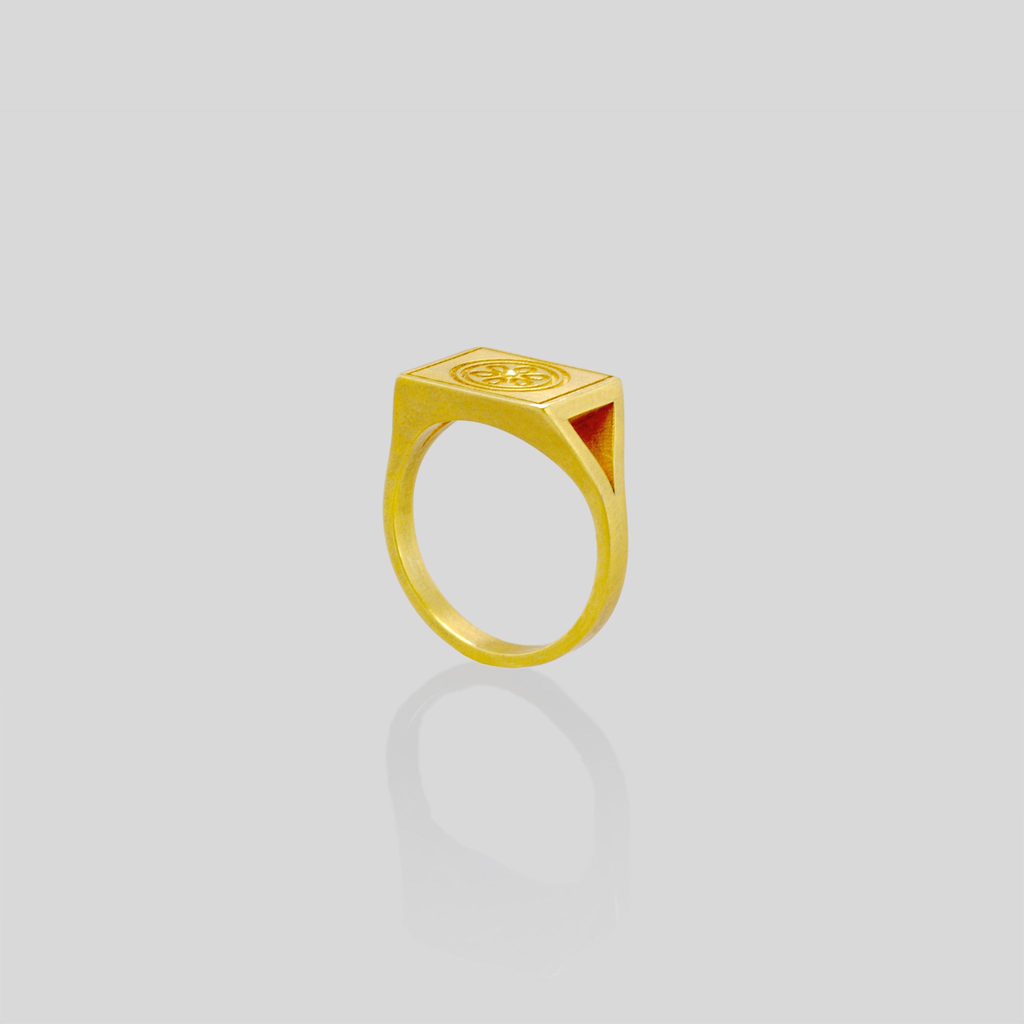 Elegant 18k gold signet ring with a square top featuring an embossed flower design, showcased against a reflective white background.