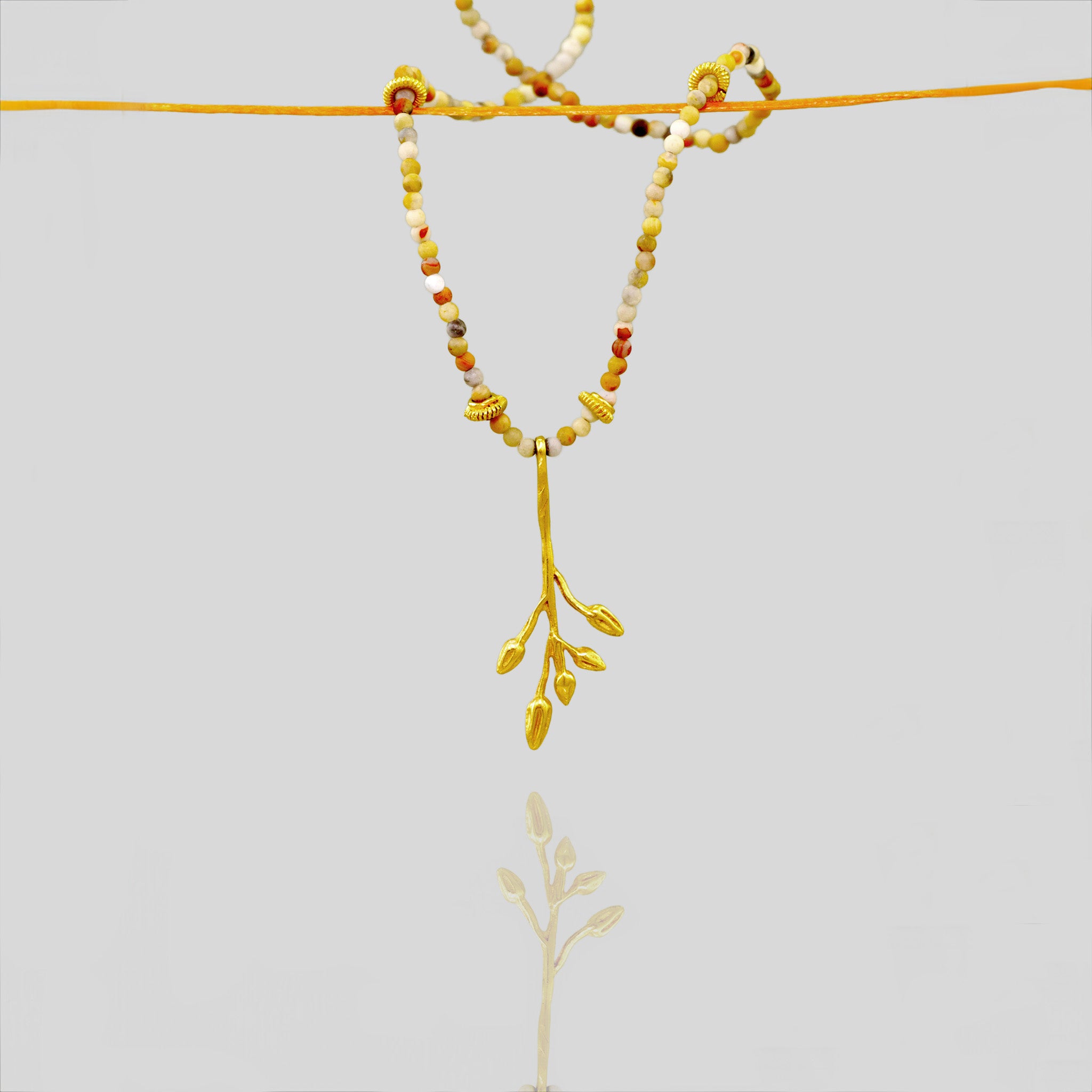Delicate yellow gold pendant designed to resemble a branch with dried seed pods, adorned with Jasper stones and gold elements for a vibrant and natural look.