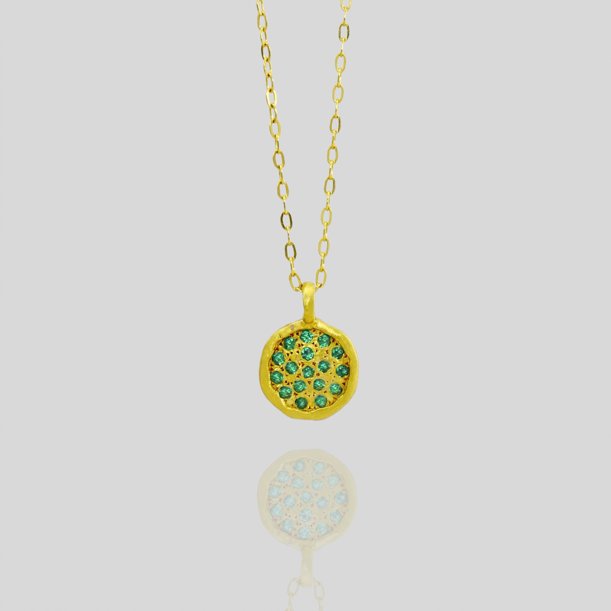close up of Starlit gold pendant, meticulously crafted from Yellow Gold with a small gold plate embellished with scattered Emeralds, mirroring the enchanting allure of a starry night.