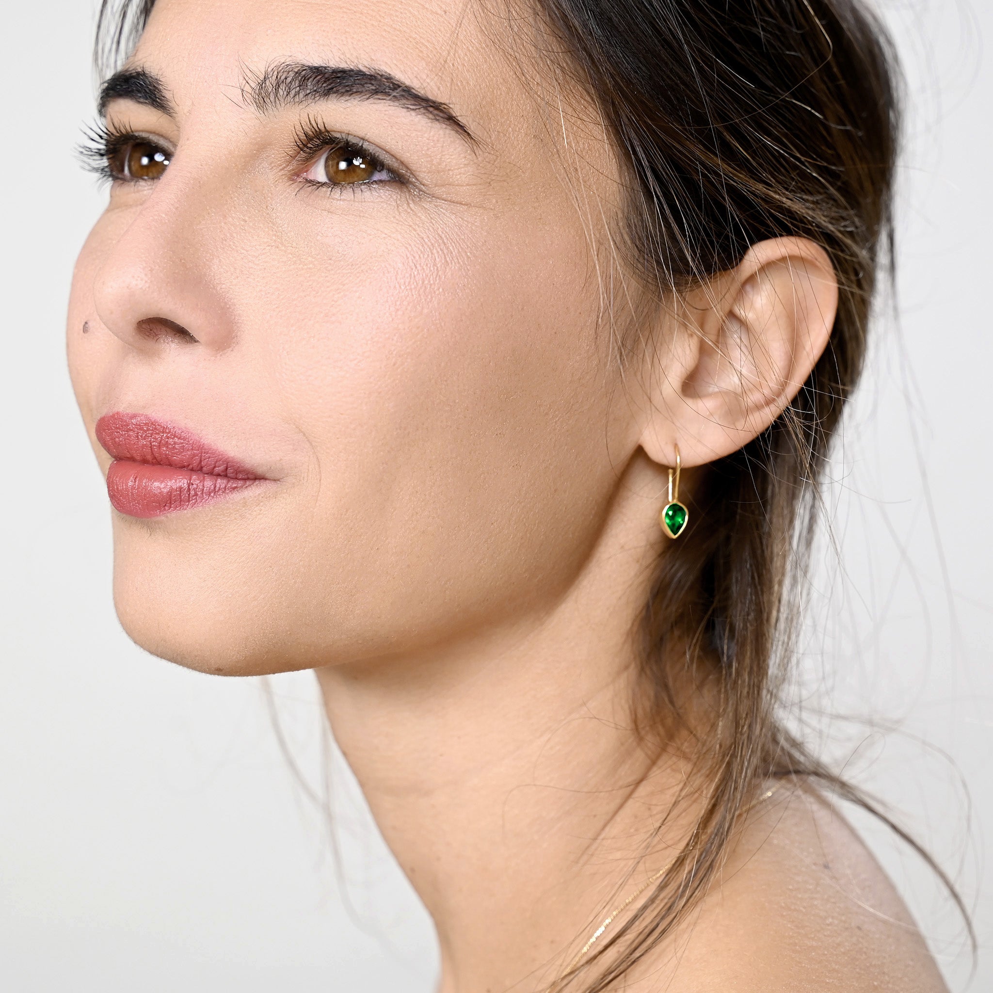 Model elegantly displaying gold drop earrings with a radiant drop-shaped emerald, enhancing spiritual harmony and adding a touch of sophistication to any attire.