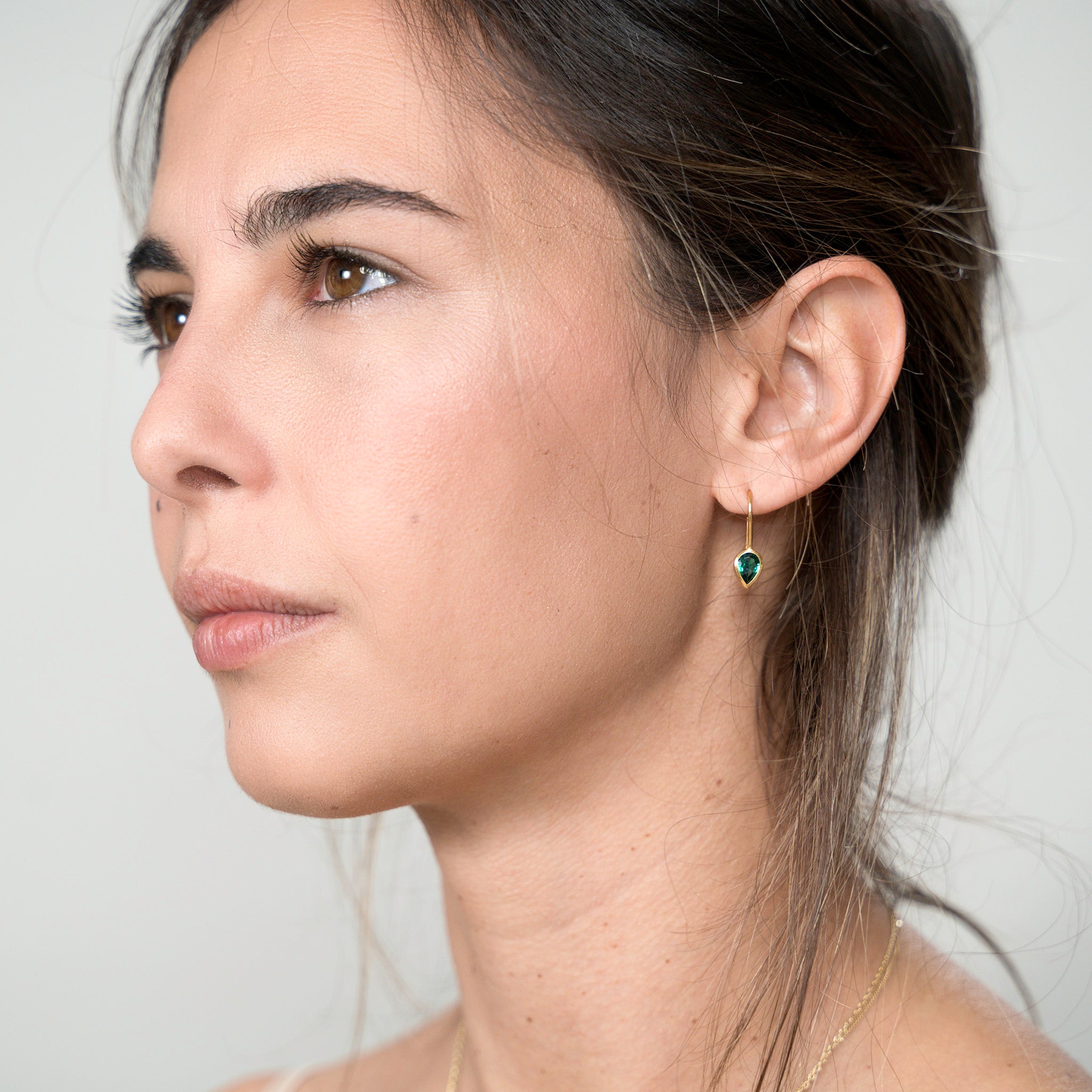 Model elegantly displaying gold drop earrings with a radiant drop-shaped emerald, enhancing spiritual harmony and adding a touch of sophistication to any attire.