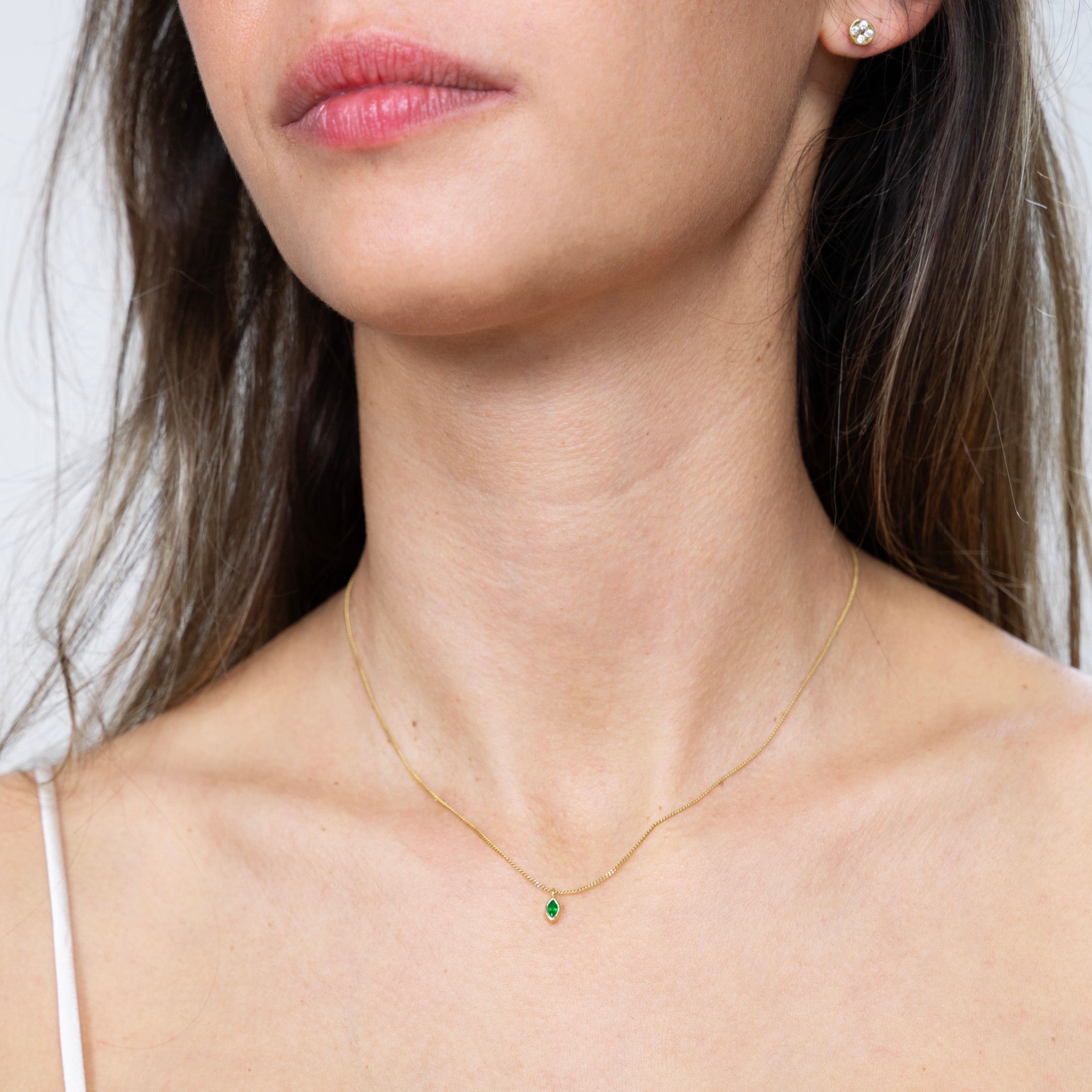 Model showcasing the elegant gold marquee pendant with a captivating emerald, infusing outfits with a touch of vibrant sophistication and symbolizing renewal, growth, and vitality.
