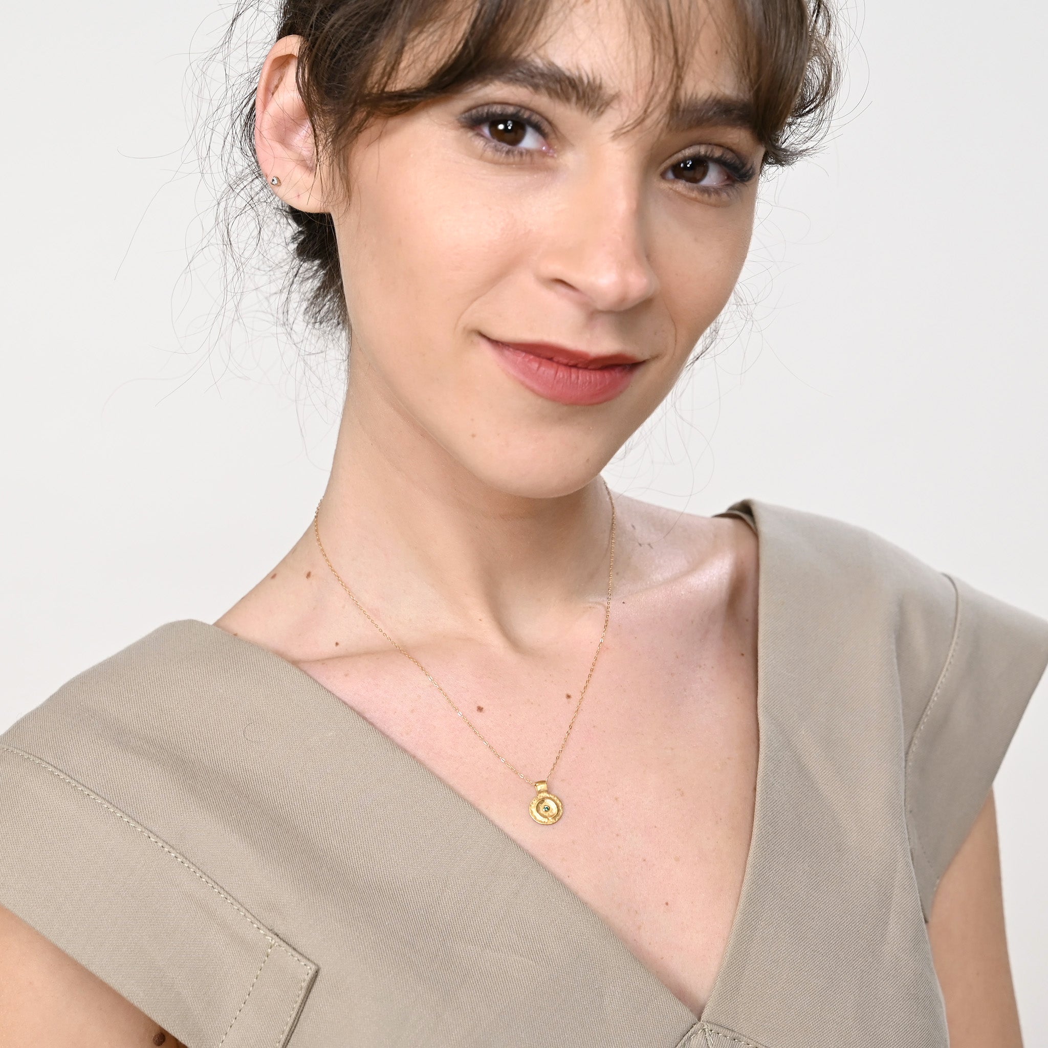 Model elegantly displaying the Pharaohs I ancient round gold pendant, featuring a central Emerald gemstone, drawing inspiration from the luxurious adornments of ancient Egyptian Pharaohs.