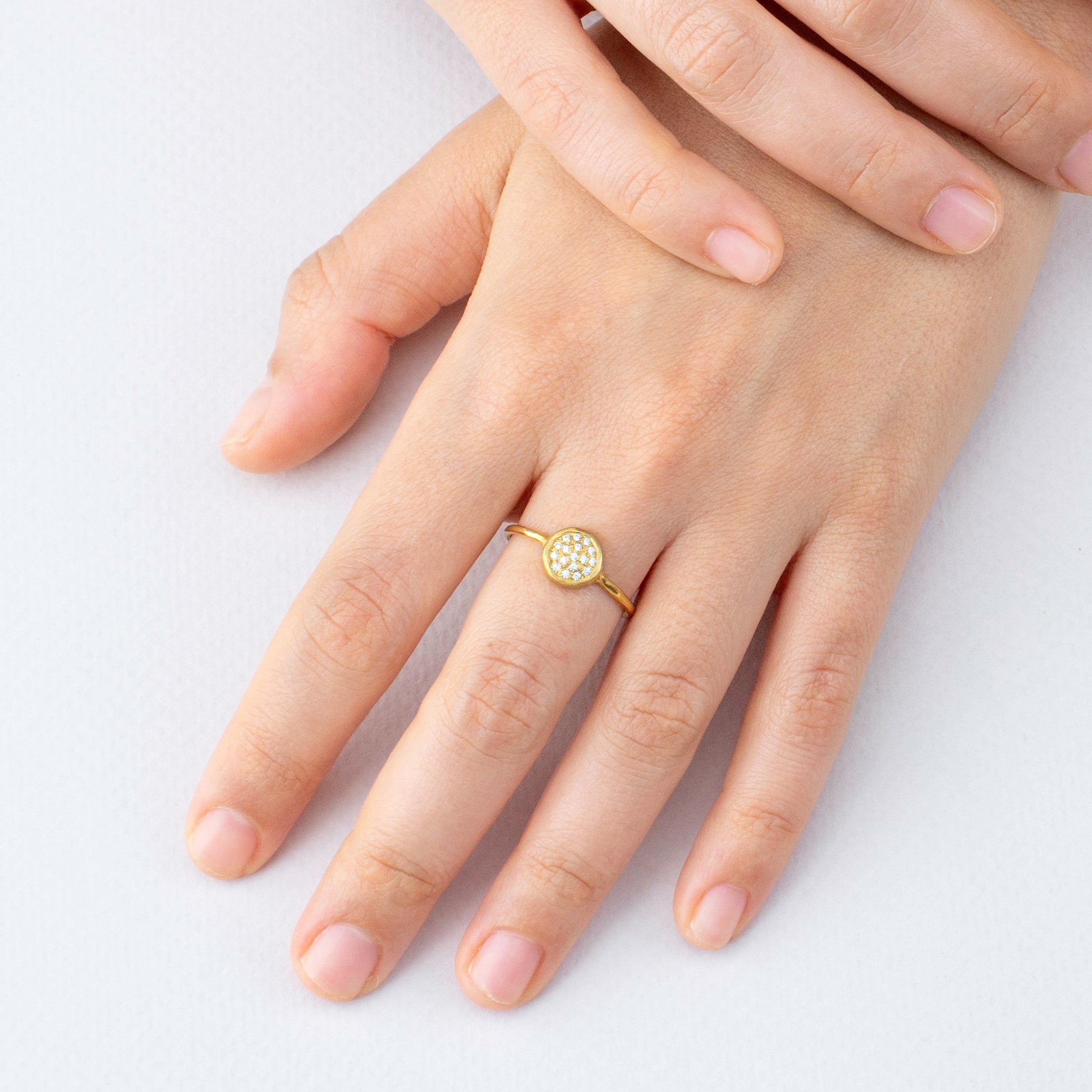 Model's hand elegantly displaying the Starlit gold ring, its circular diamond-encrusted plate shimmering brilliantly, reminiscent of a clear, starry night.
