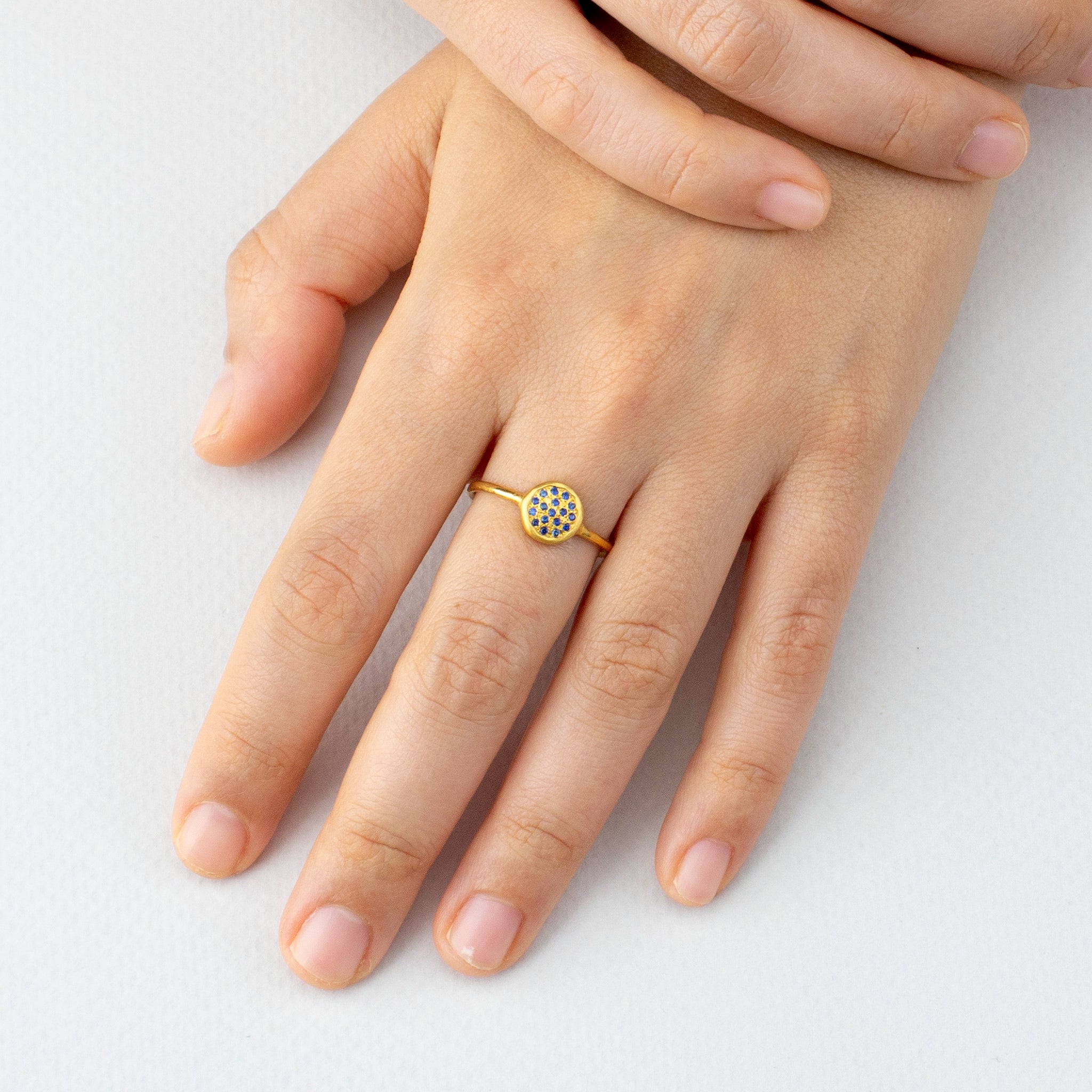 Model's hand elegantly displaying the Starlit gold ring, its circular sapphires-encrusted plate shimmering brilliantly, reminiscent of a clear, starry night.