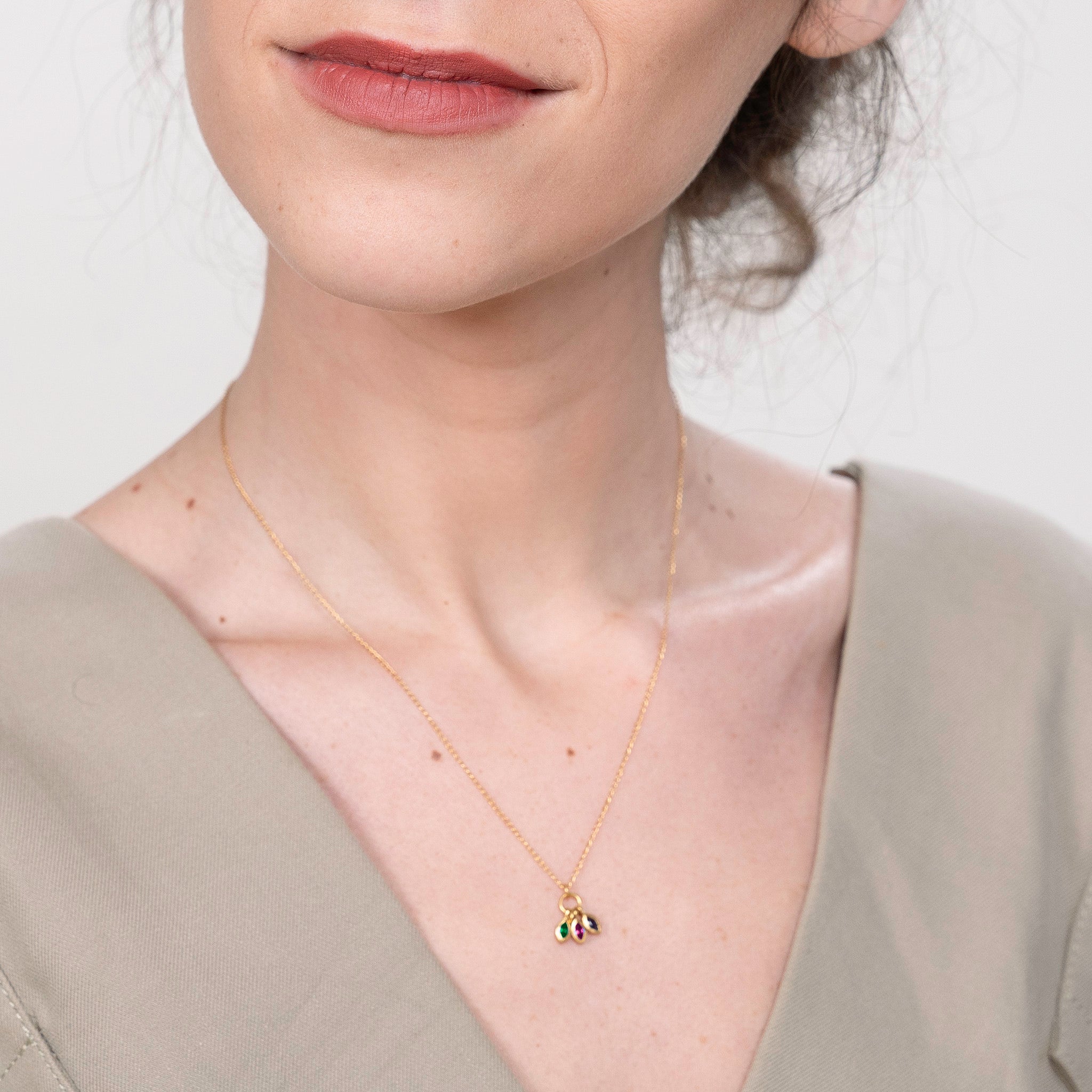 Model elegantly wearing a gold marquee pendant, featuring a Ruby, Emerald, and Sapphire that create a mesmerizing blend of color and light, adding a touch of sophisticated charm to any ensemble.