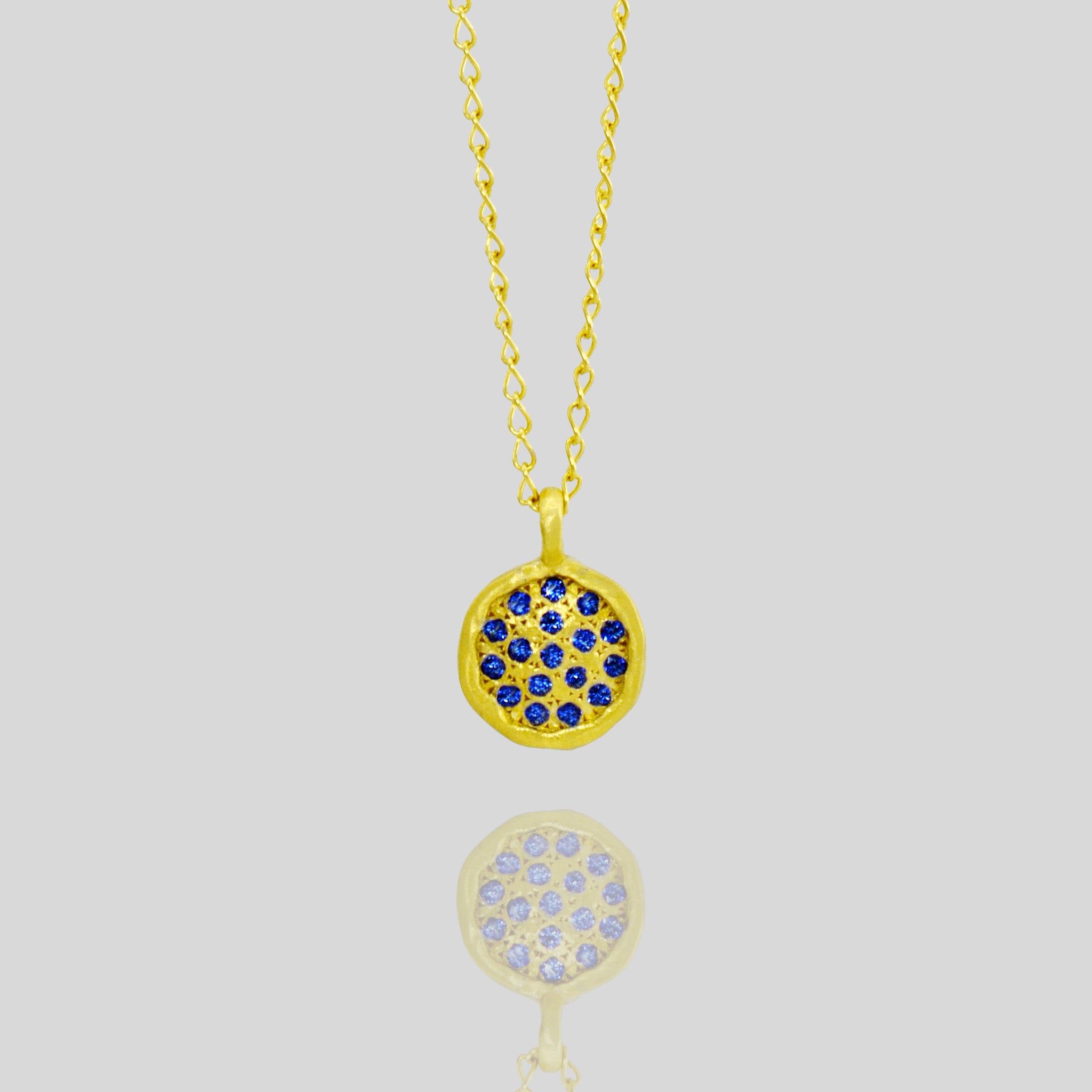 Close up of Starlit gold pendant, exquisitely handmade from Yellow Gold, featuring a small gold plate adorned with scattered Sapphires, evoking visions of a vibrant starry night.