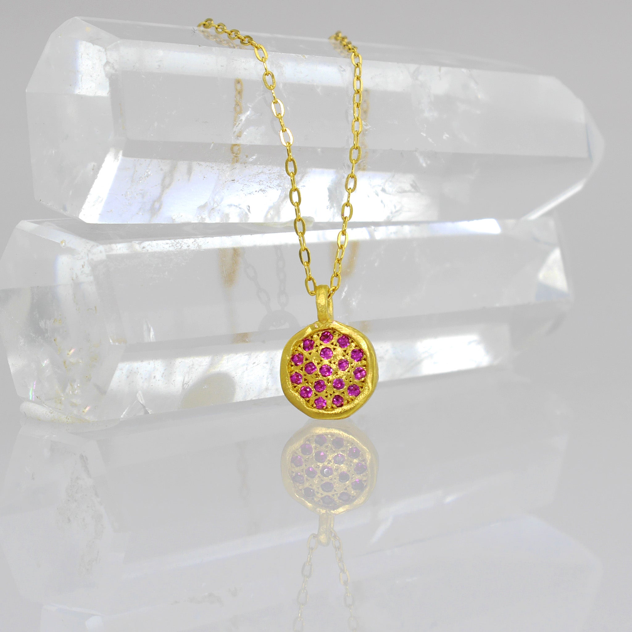 Close up of Starlit gold pendant, exquisitely handmade from Yellow Gold, featuring a small gold plate lavishly adorned with scattered Rubies, evoking visions of a vibrant starry night.