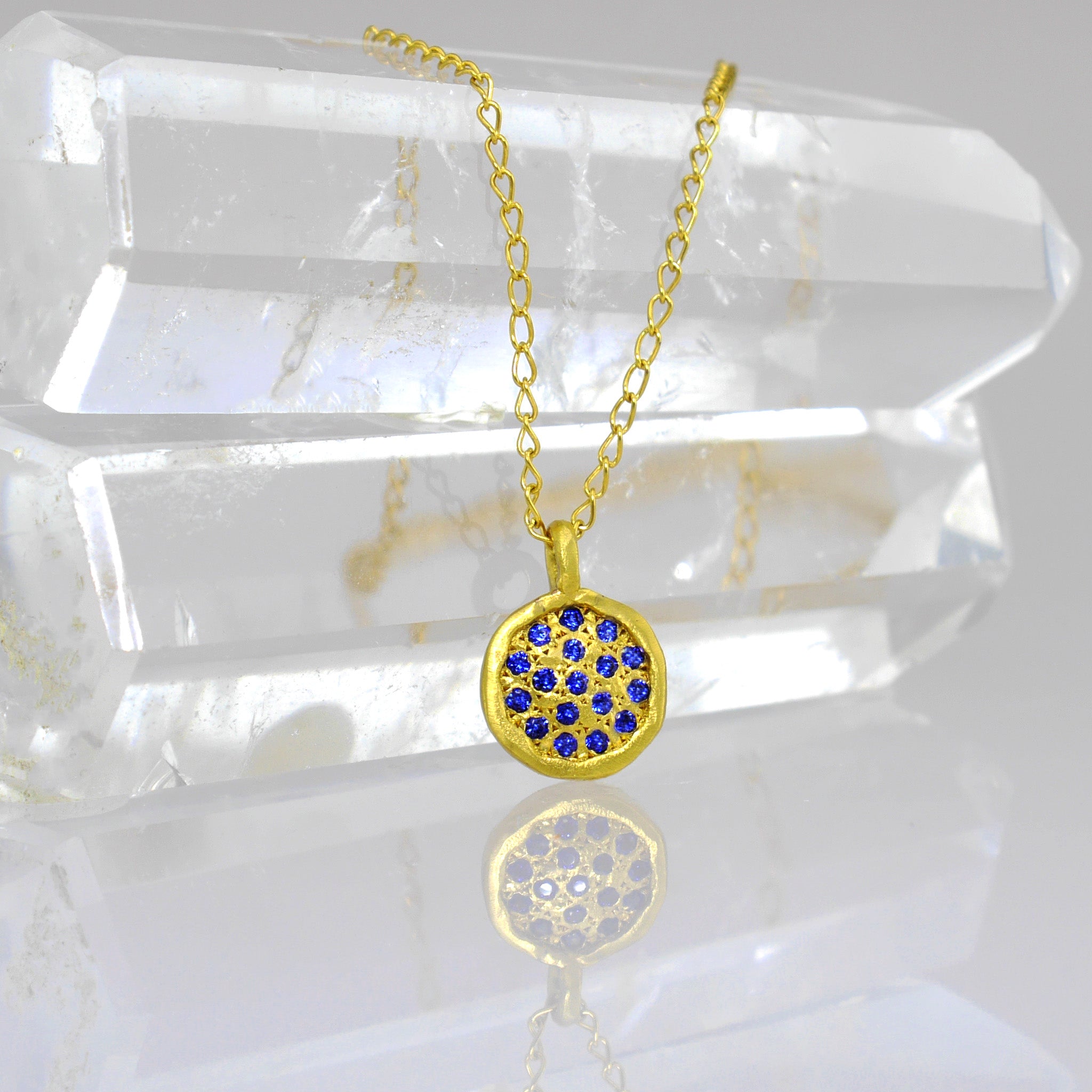 Detail of Starlit gold pendant, exquisitely handmade from Yellow Gold, featuring a small gold plate adorned with scattered Sapphires, evoking visions of a vibrant starry night.