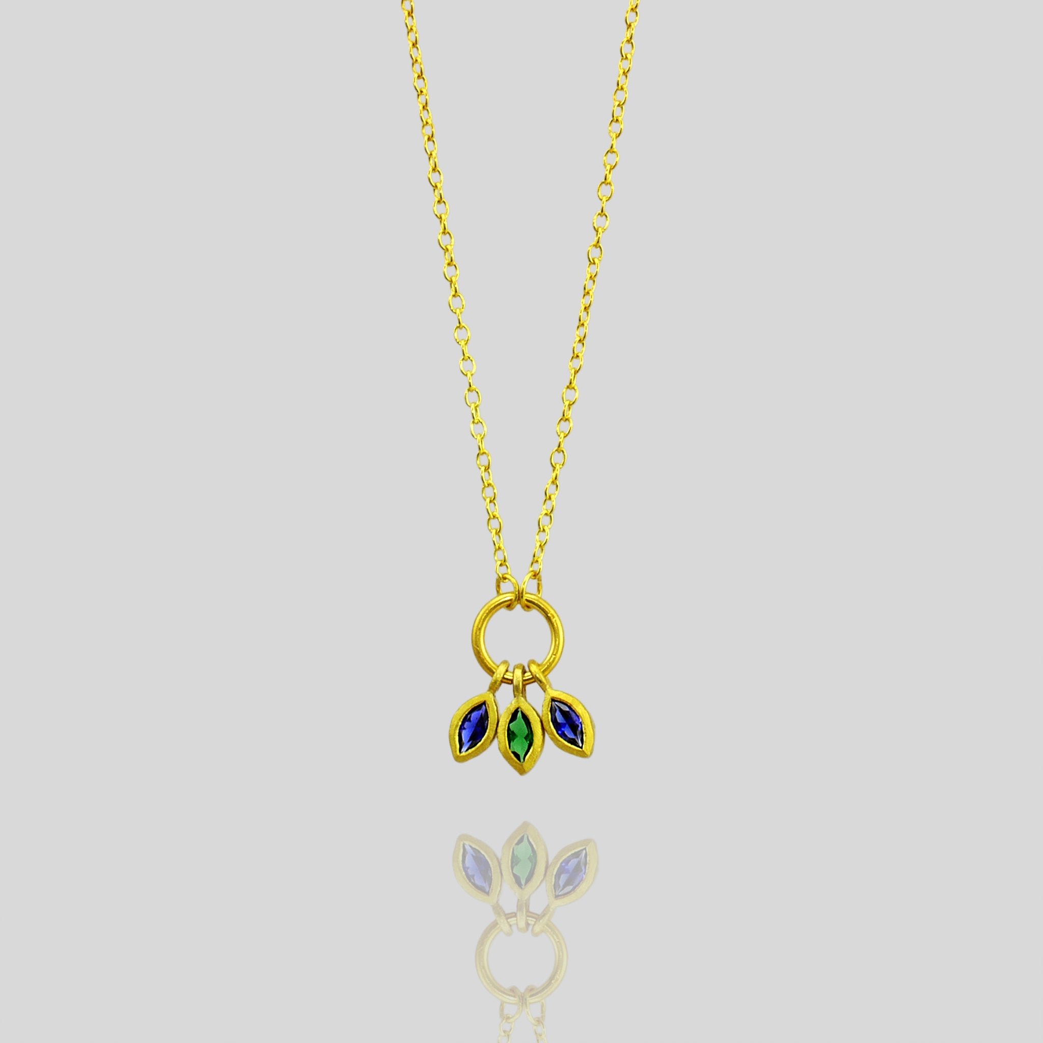 Close up of an 18k Gold Marquee pendant with three precisely cut gemstones, an emerald and two sapphires, combining to offer a vibrant mix of color and elegance.
