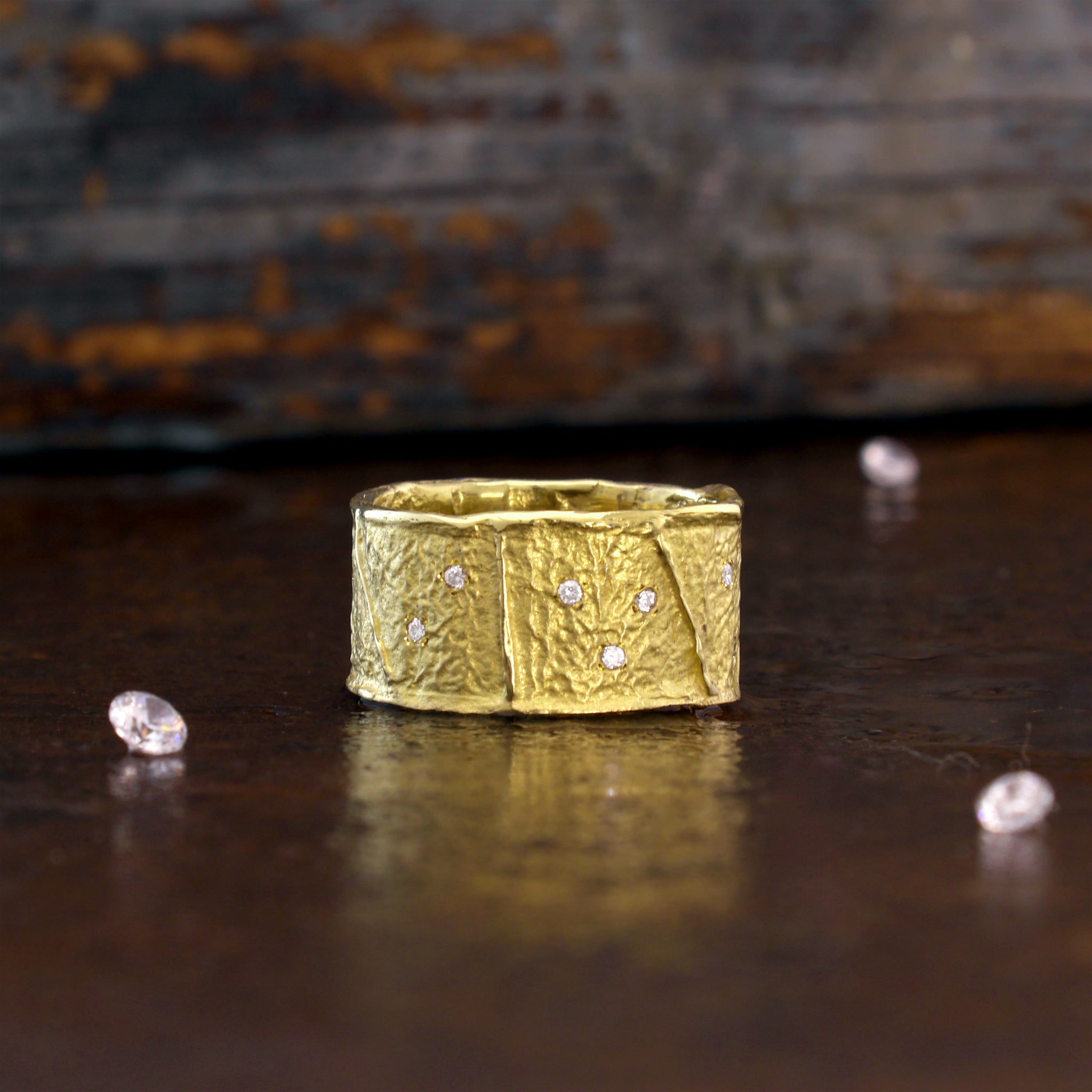 A stunning 18k Yellow Gold Ring, on a dark rustic background, featuring a unique wrinkled texture inspired by ancient Egyptian artistry, elegantly adorned with tiny sparkling diamonds for a timeless charm.